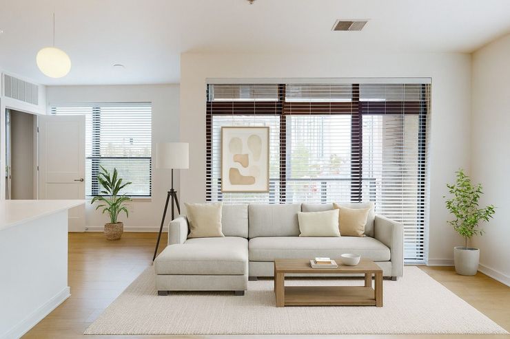 Here at Vim + Vigor Lofts in Wisconsin. A bright living room features a cozy cream sofa, warm wood flooring, large windows, modern décor, and inviting natural light.