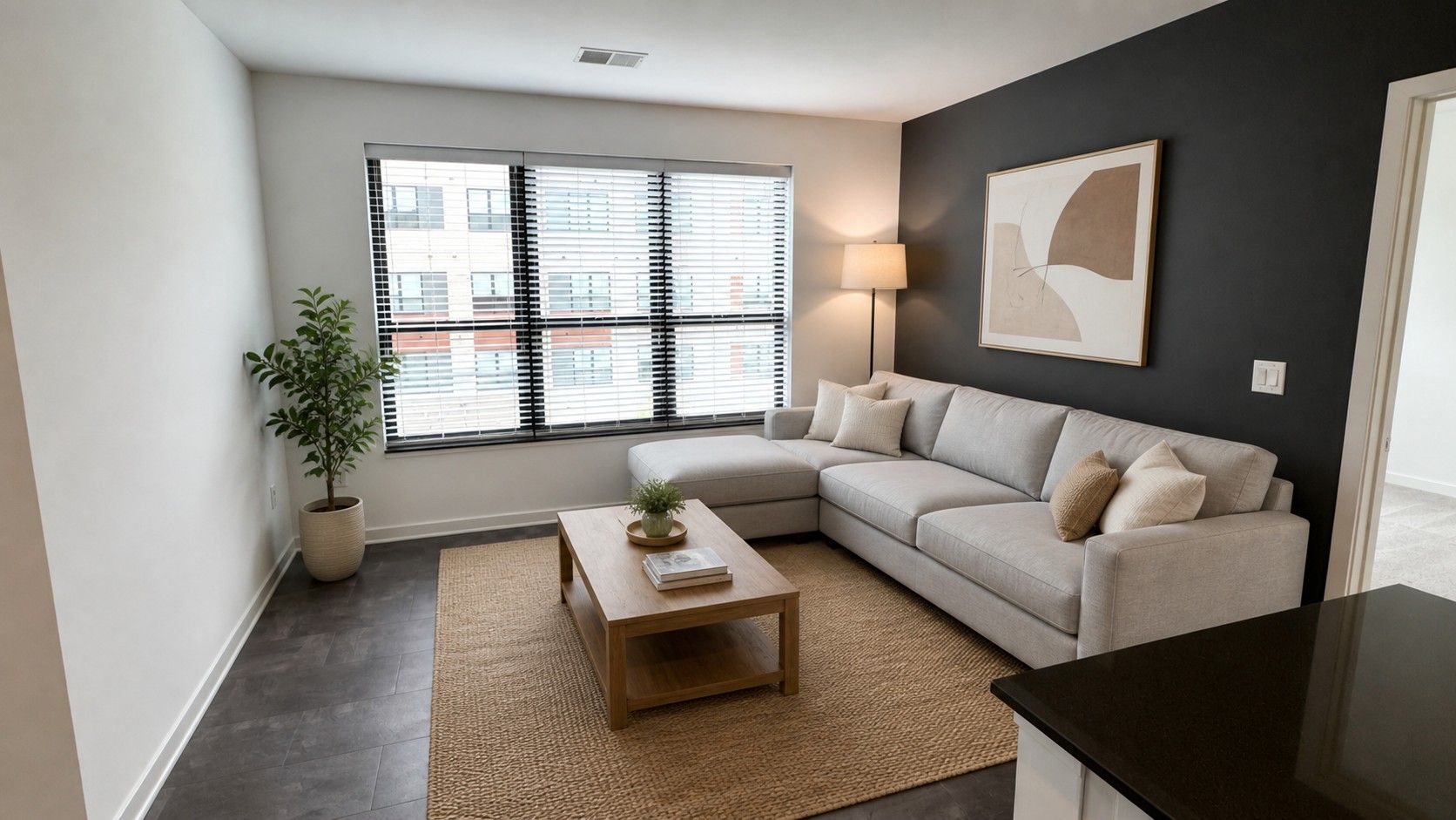 Here at Vim + Vigor Lofts in Wisconsin. A cozy living room features a cream sectional, warm wood coffee table, textured rug, large windows, and a modern dark accent wall.
