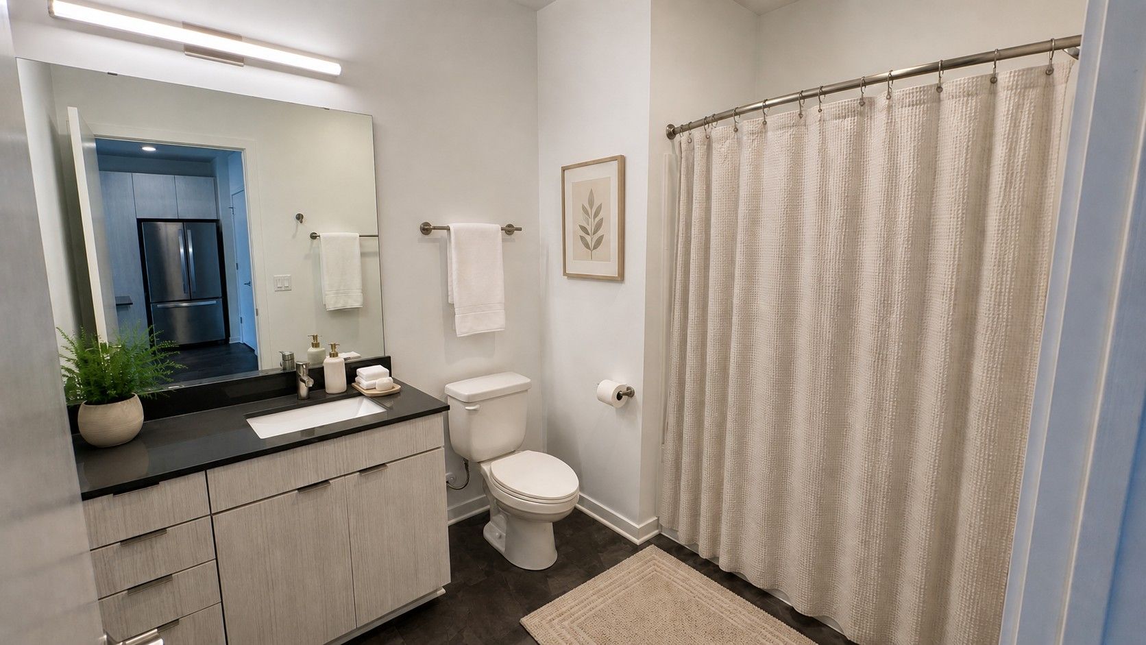 Here at Vim + Vigor Lofts in Wisconsin. A bright bathroom features a modern vanity, neutral shower curtain, soft towels, warm décor, and clean contemporary finishes.
