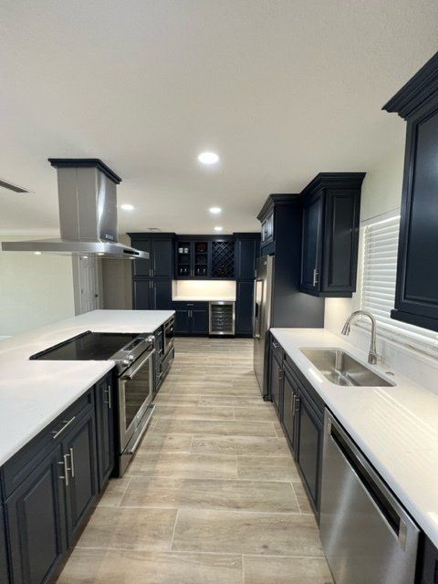 Navy blue kitchen with white countertops, stainless steel appliances, and light wood-look flooring.