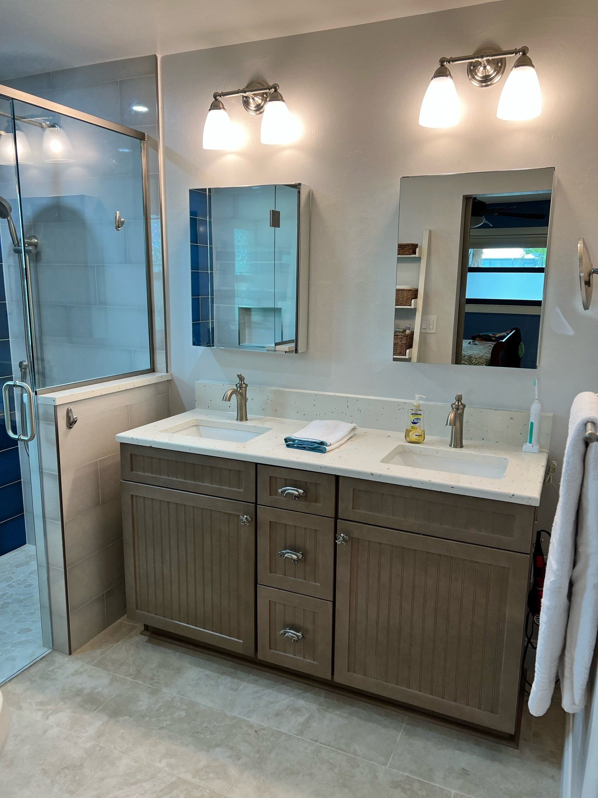 Bathroom with a double vanity, two mirrors, and a glass-enclosed shower. Light gray cabinets and walls.