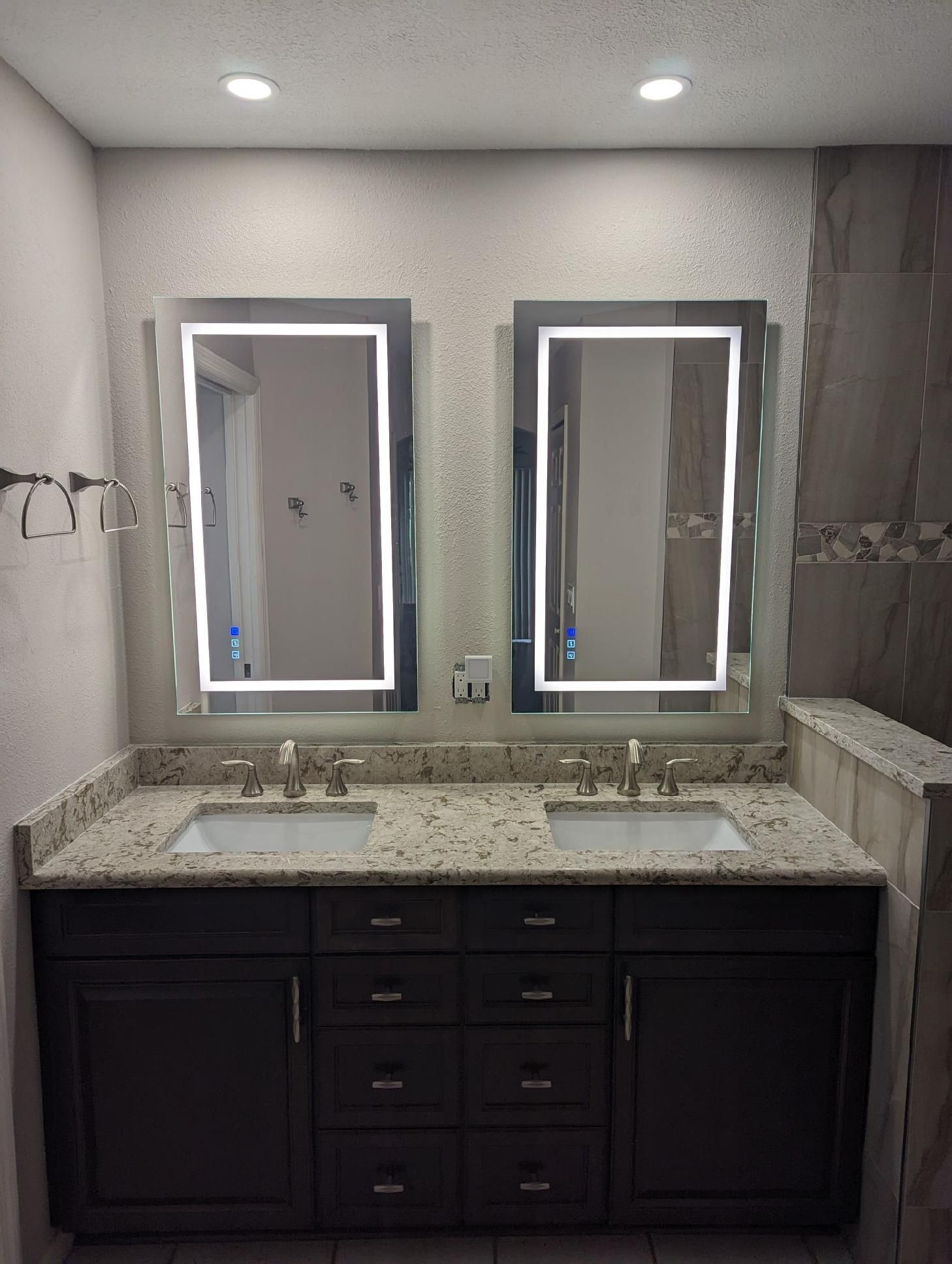 Bathroom with two sinks, illuminated mirrors, granite countertop, and dark cabinets.