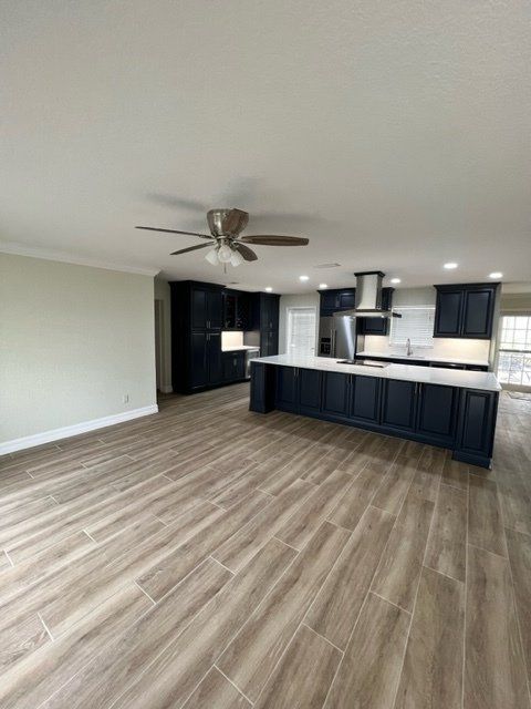 Open-concept kitchen with dark blue cabinets, white countertops, stainless steel appliances, and wood-look tile floors.