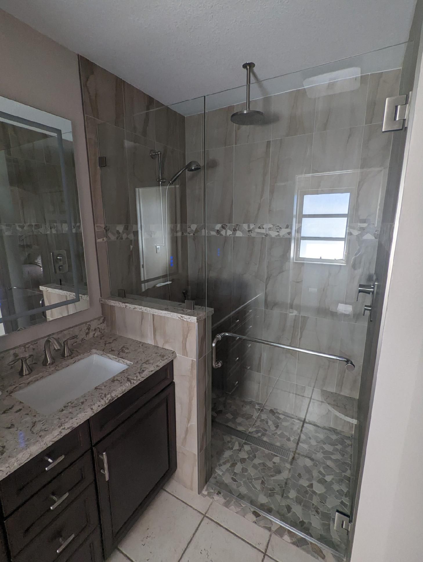 Bathroom with brown vanity, stone shower, and glass door.