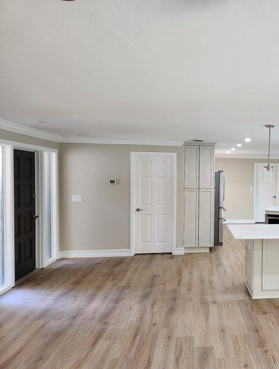 Empty, open-concept room with light wood floors, white cabinets, and a kitchen island.