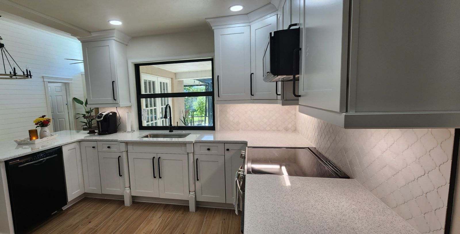 White kitchen with black appliances, white cabinets, and a window overlooking a yard.