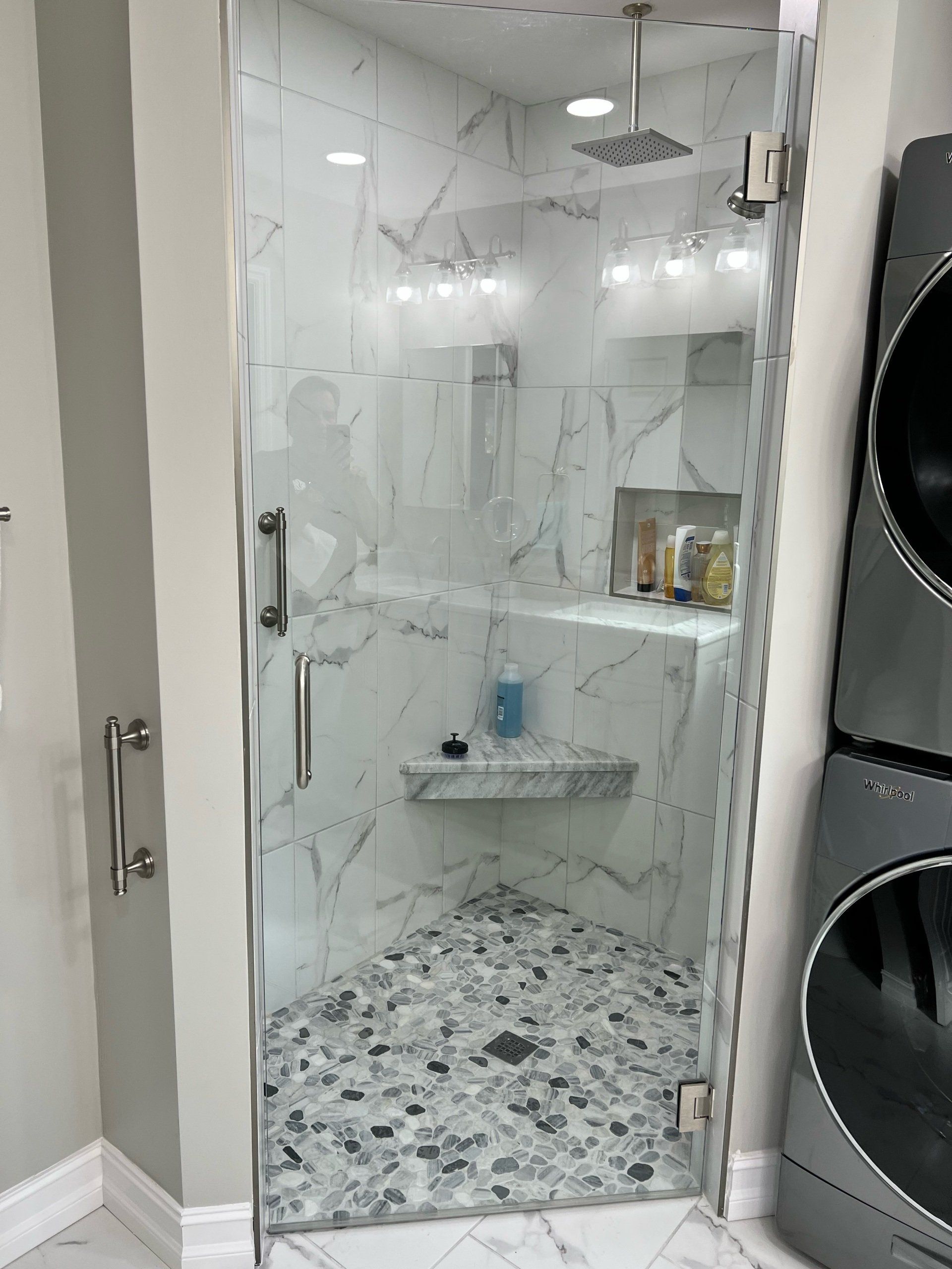 Glass door shower with marble tiles and pebble floor.