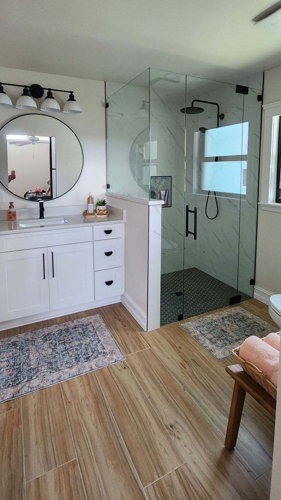 Modern bathroom with a glass shower, white vanity, and wood-look flooring.