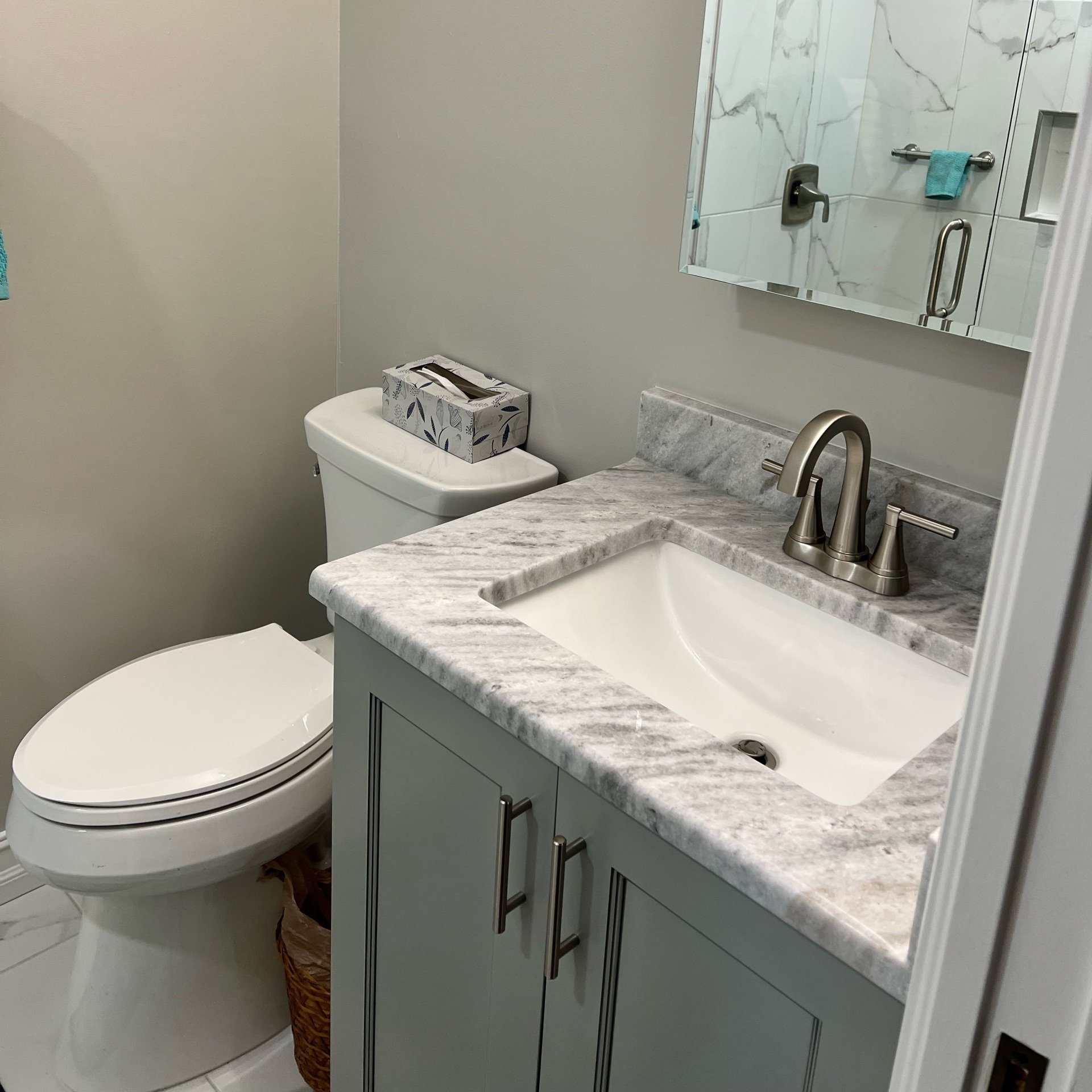 Bathroom with gray vanity, white sink, toilet, and tissue box. Marble-look countertop.