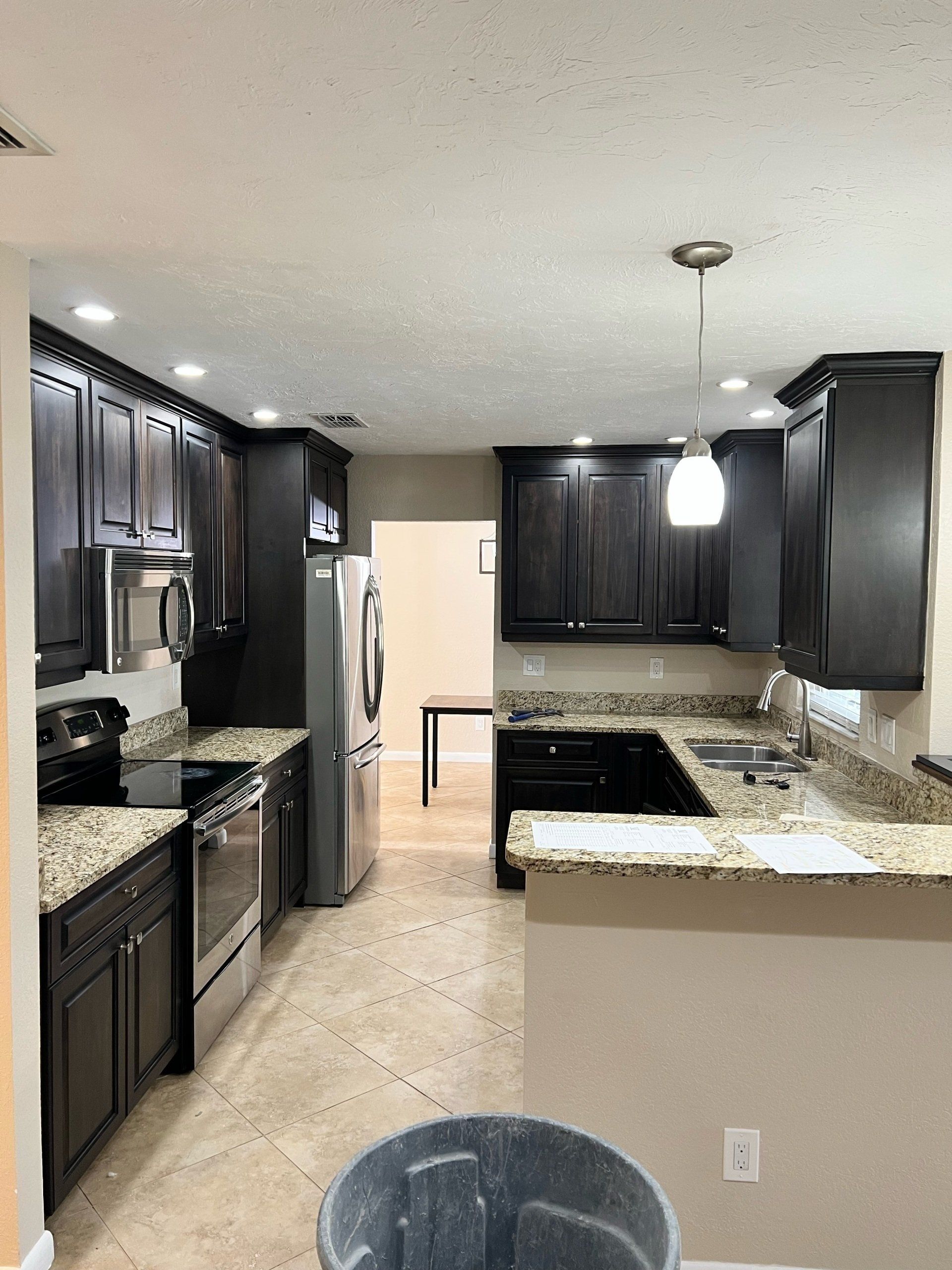 Dark-colored kitchen cabinets, granite countertops, stainless steel appliances, and a trash can.