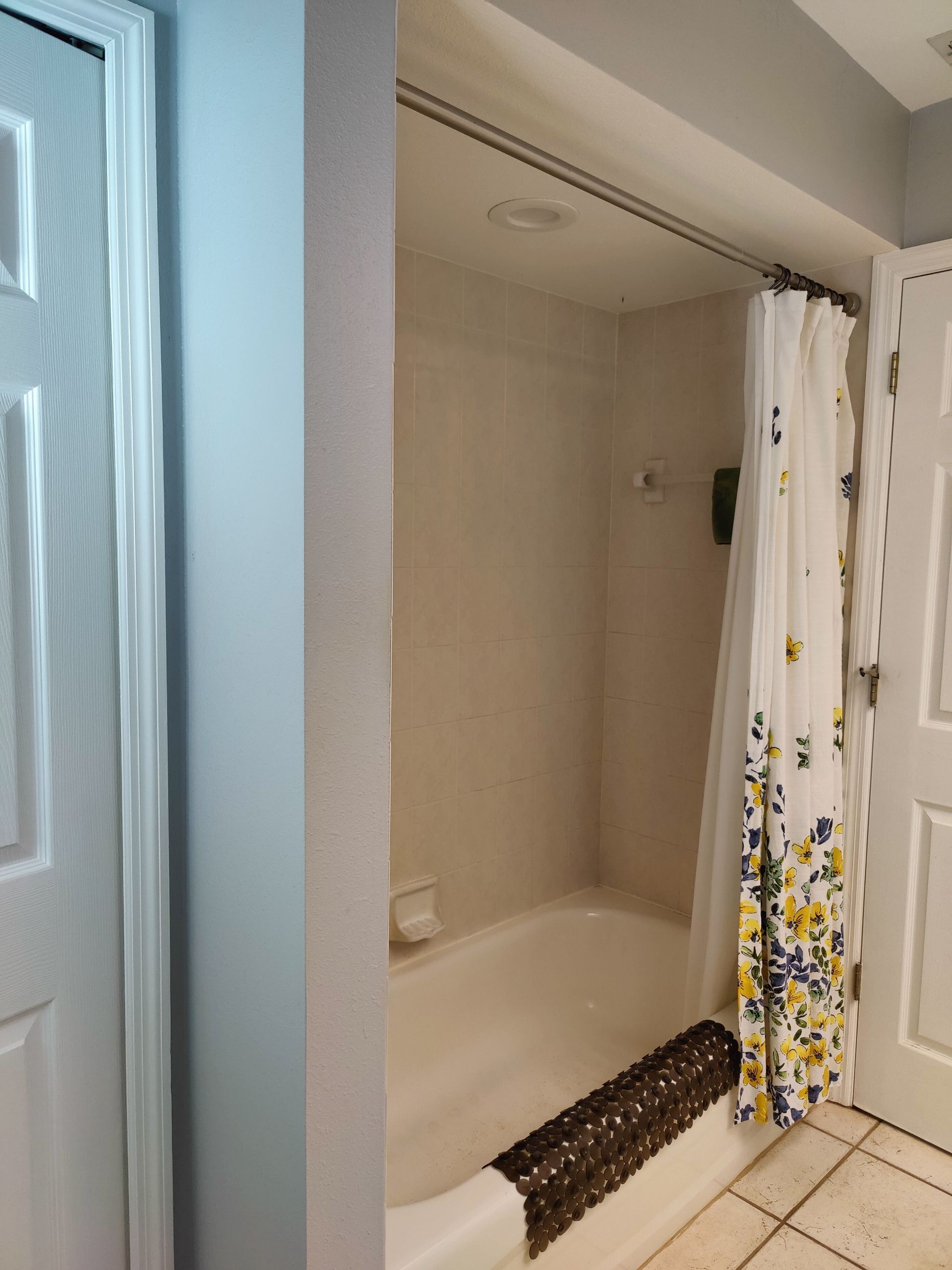 Bathroom with a white tub, tan walls, a patterned shower curtain, and a brown rug.
