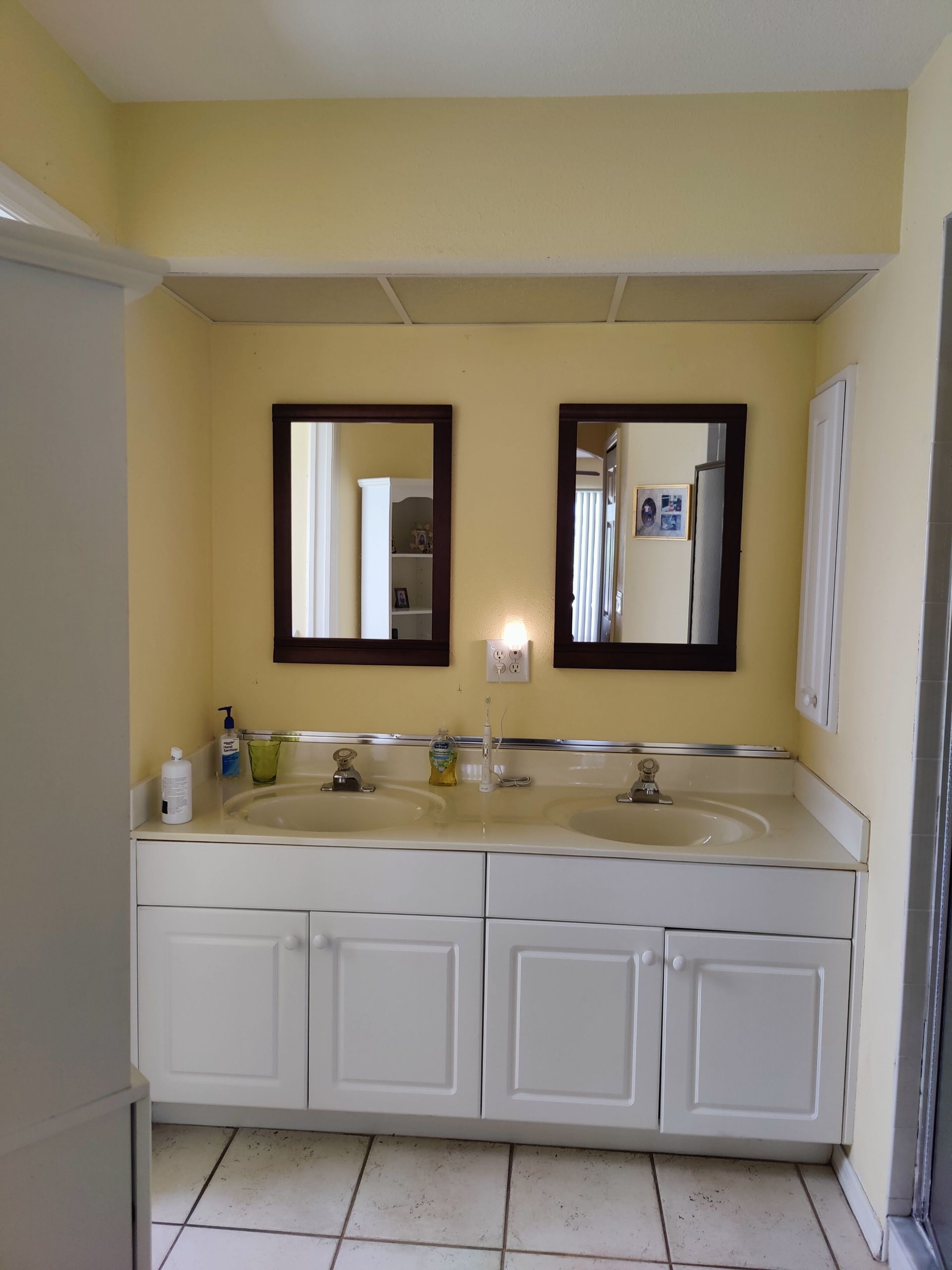 Bathroom with double sinks, mirrors, and white cabinets. Yellow walls and a tiled floor.