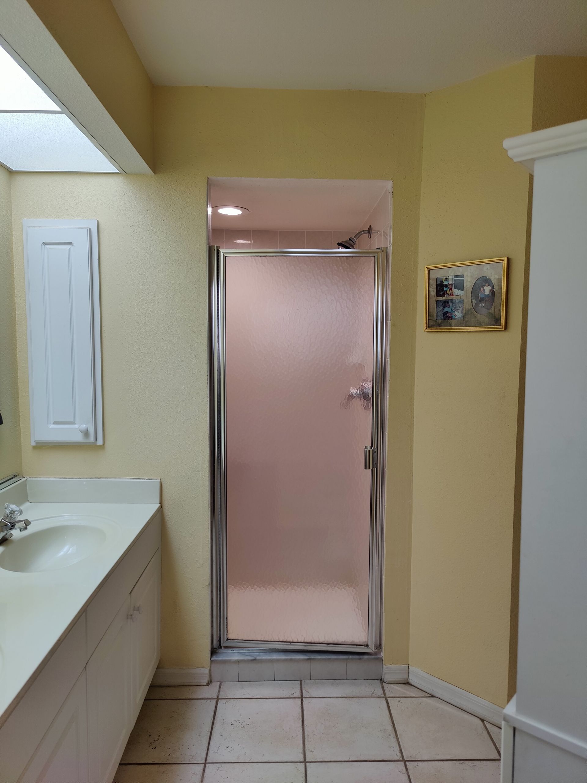 Bathroom with a shower, sink, and cabinet. Yellow walls, beige floor tiles.