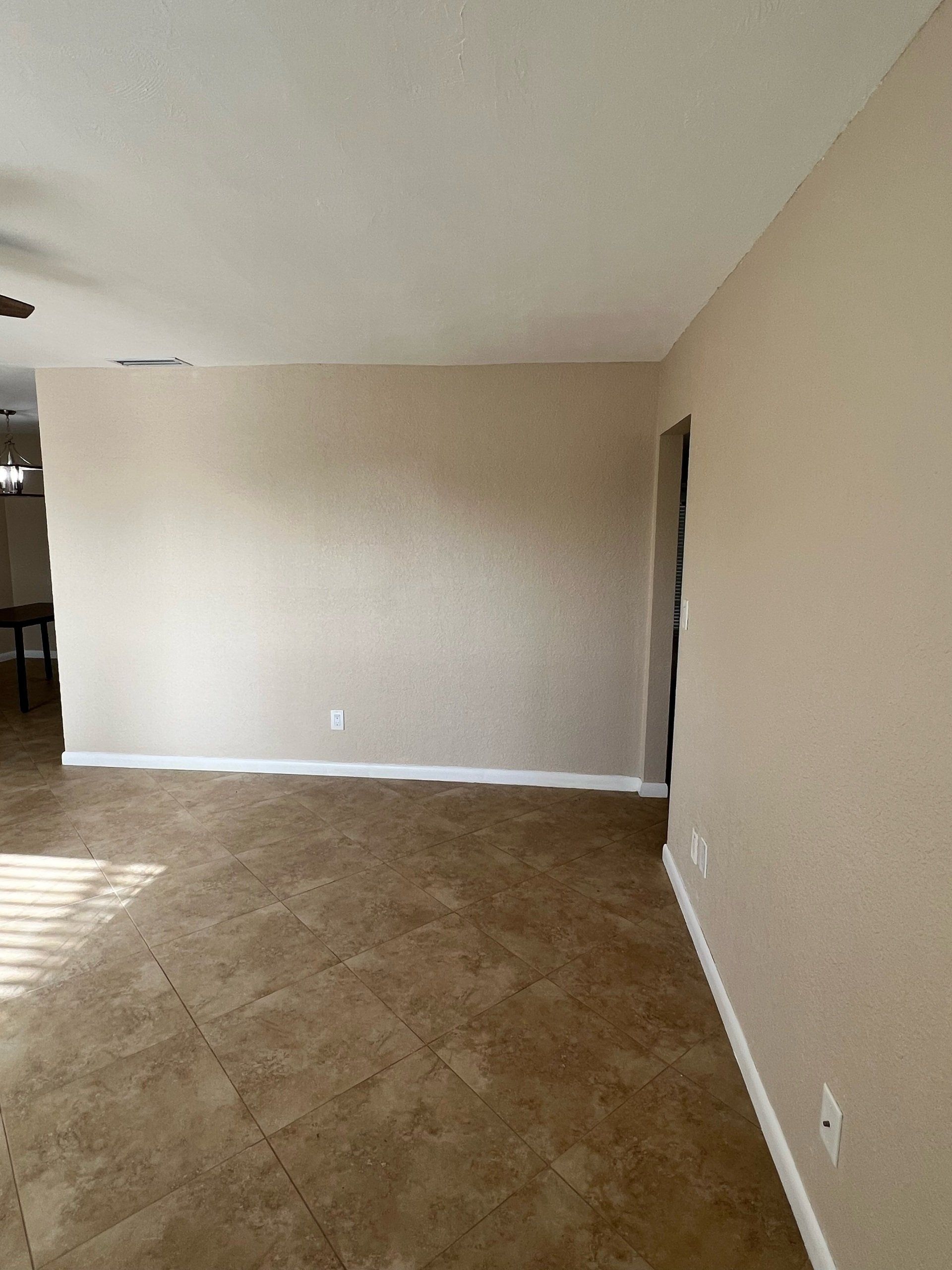 Empty living room with beige walls, brown flooring, and a doorway.