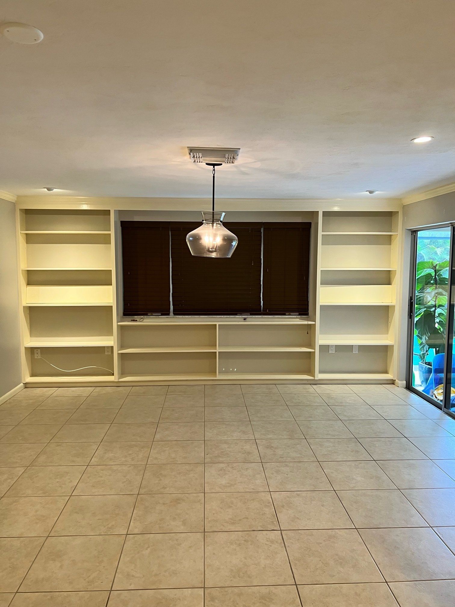 Empty room with built-in white bookshelves, brown blinds, and a pendant light, with tile flooring.