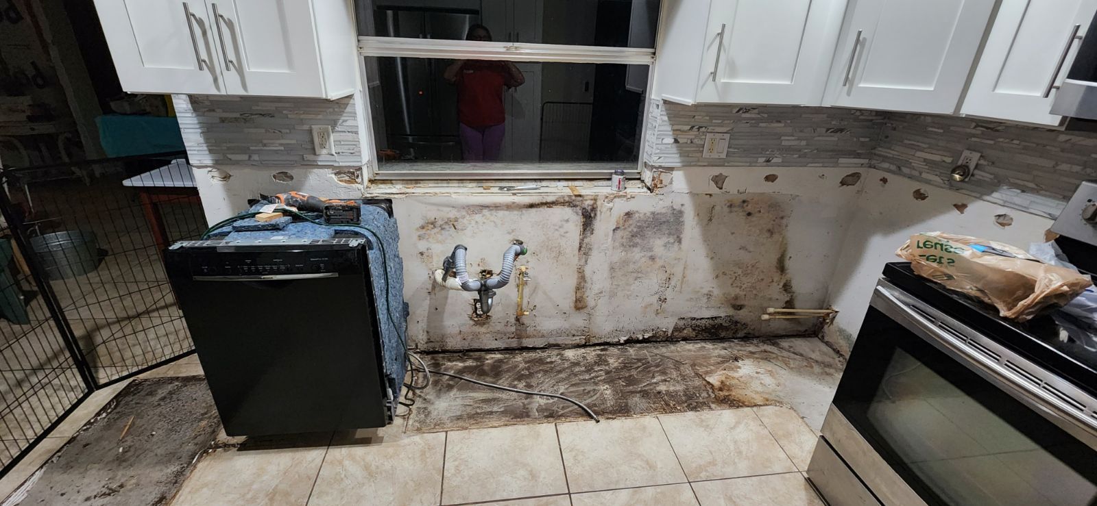 Kitchen undergoing renovation, exposed wall, black dishwasher, cabinets, stove, and window.