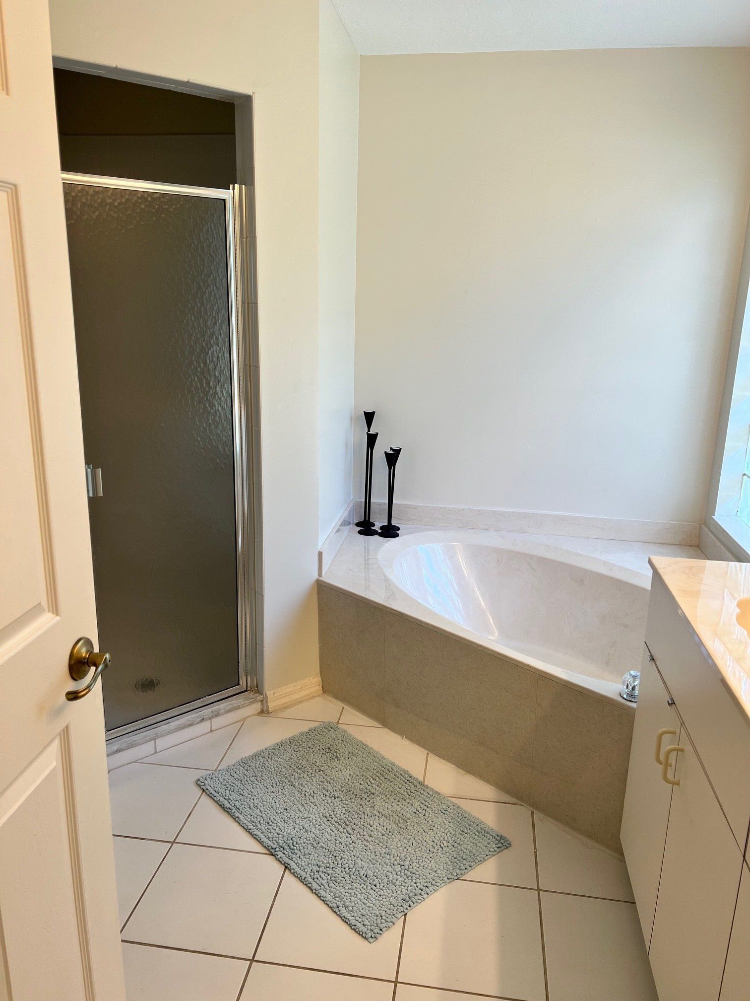 Bathroom with a shower, corner bathtub, vanity, and light blue bath mat.