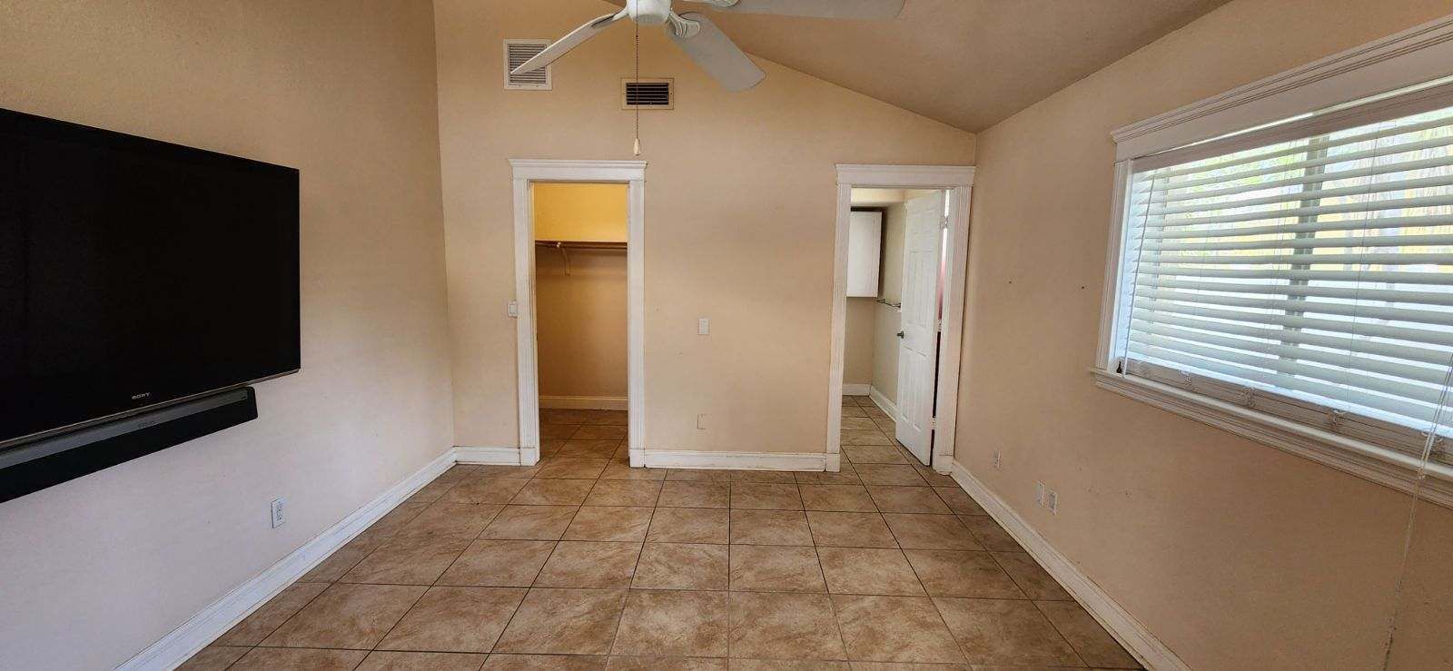 Bedroom with tile floor, closet, bathroom door, and mounted TV.