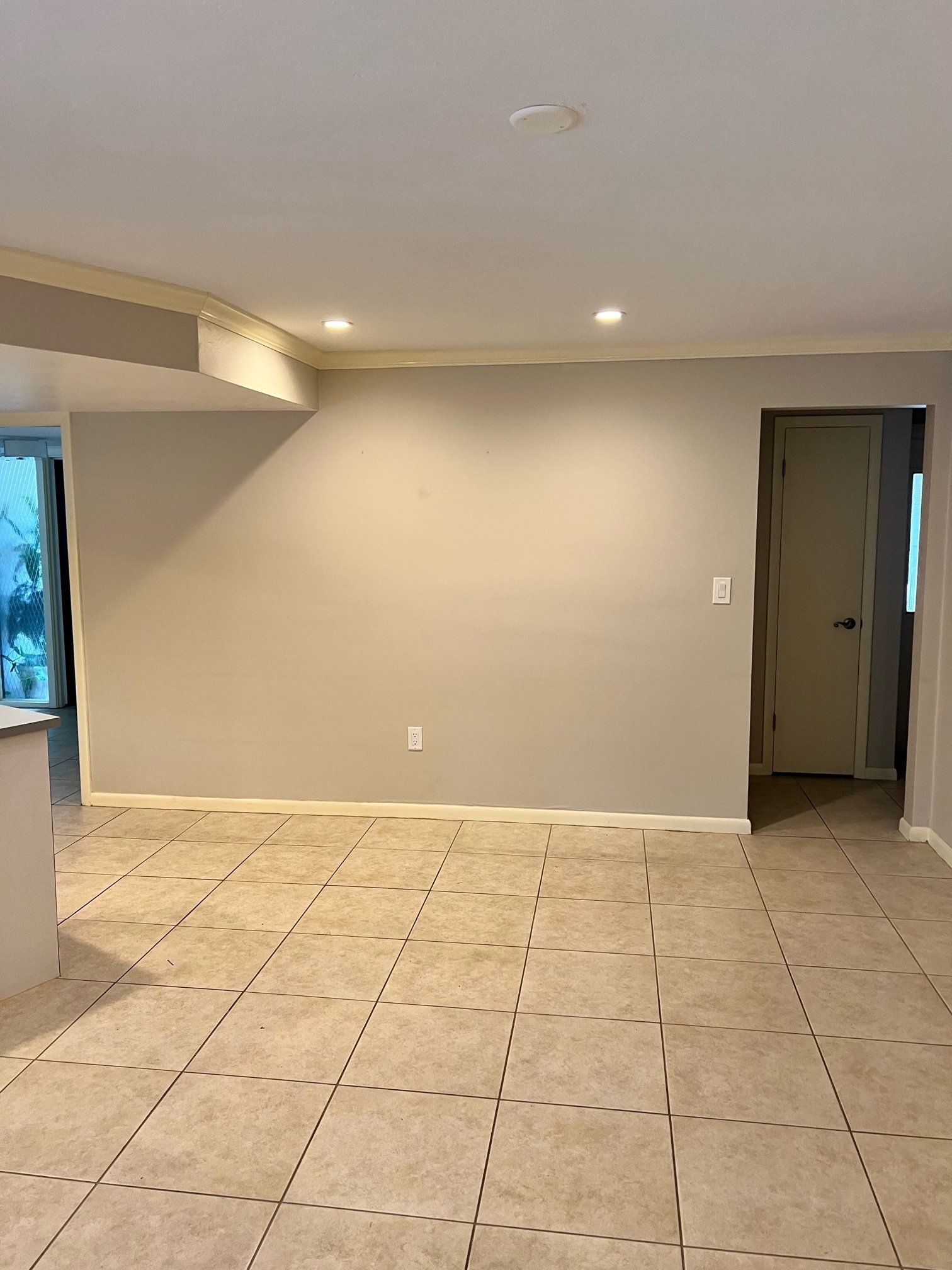 Empty room with beige walls, tan tile floor, recessed lighting, and a doorway.