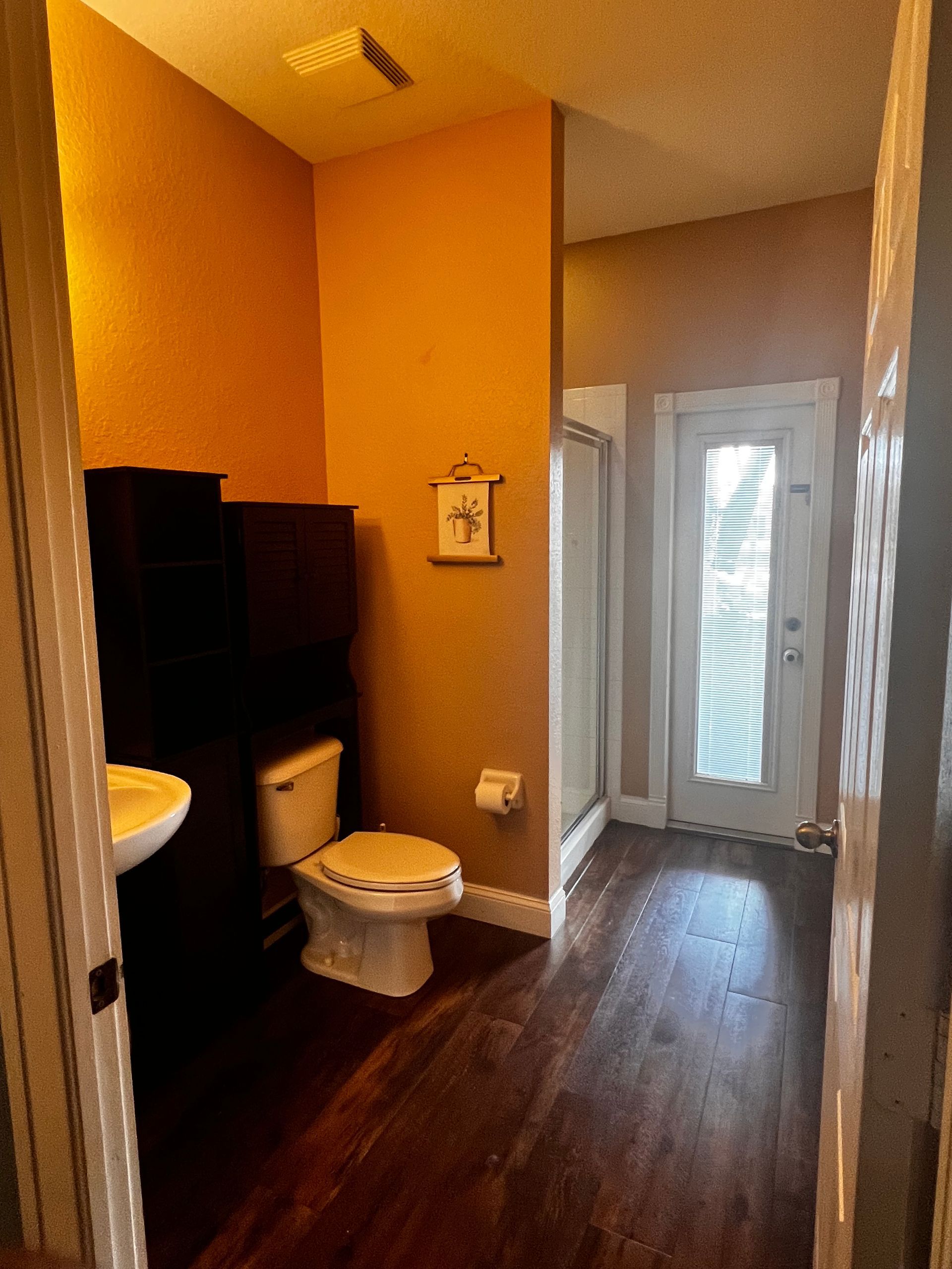 Bathroom with dark wood floor, orange walls, toilet, sink, and glass shower door.