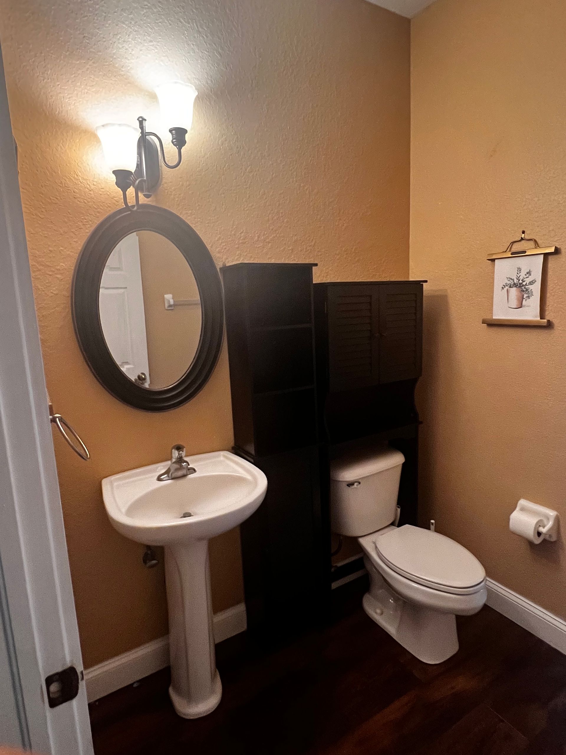 Small bathroom with a pedestal sink, toilet, and dark storage cabinet; gold-colored walls.