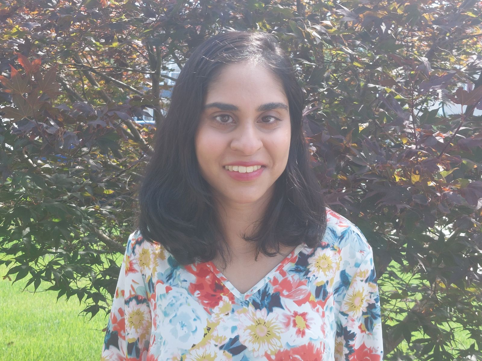 Woman with dark hair in striped shirt against a background of green foliage and flowers.