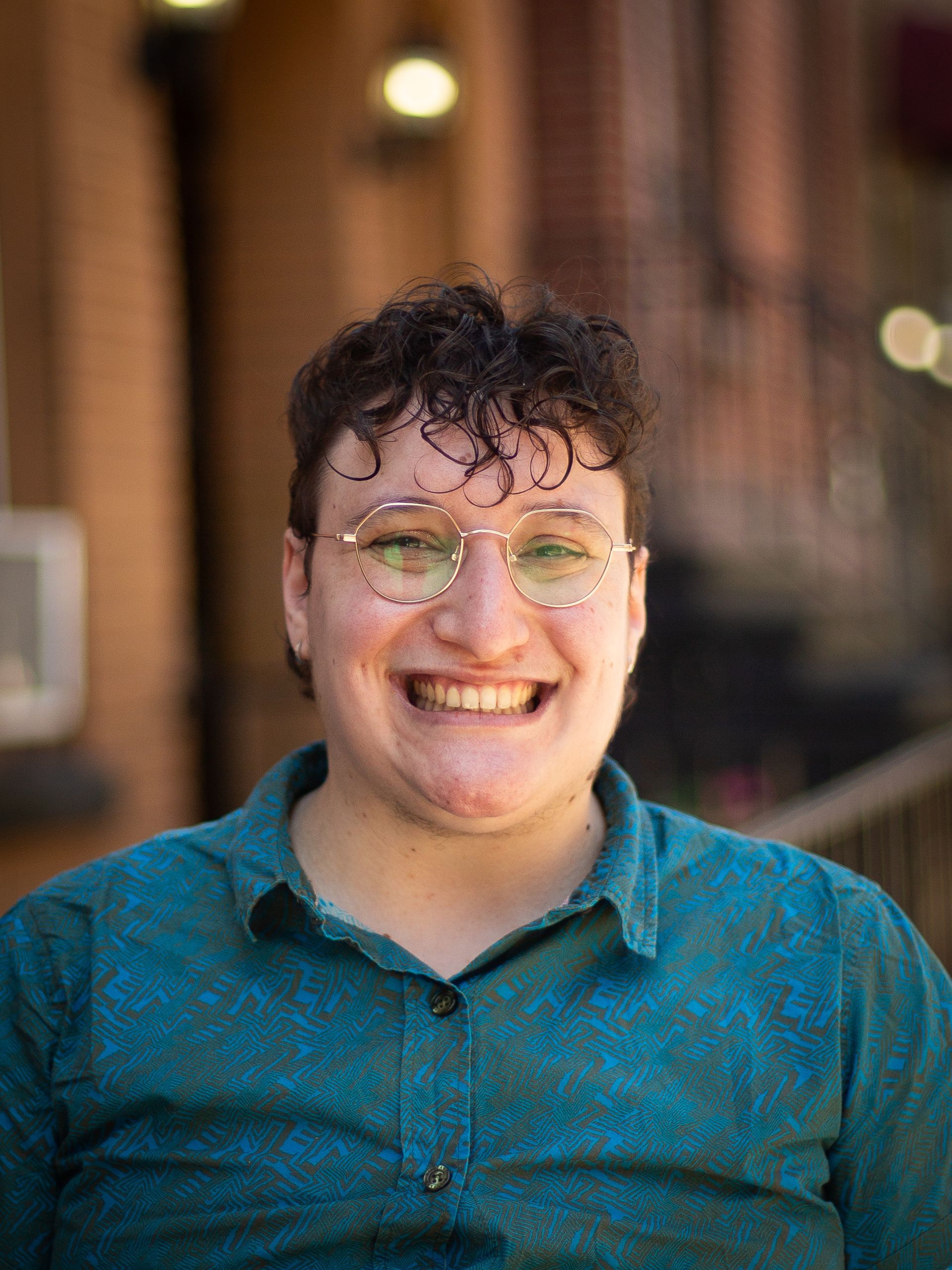 Woman with brown hair, smiling, in front of a brick building.