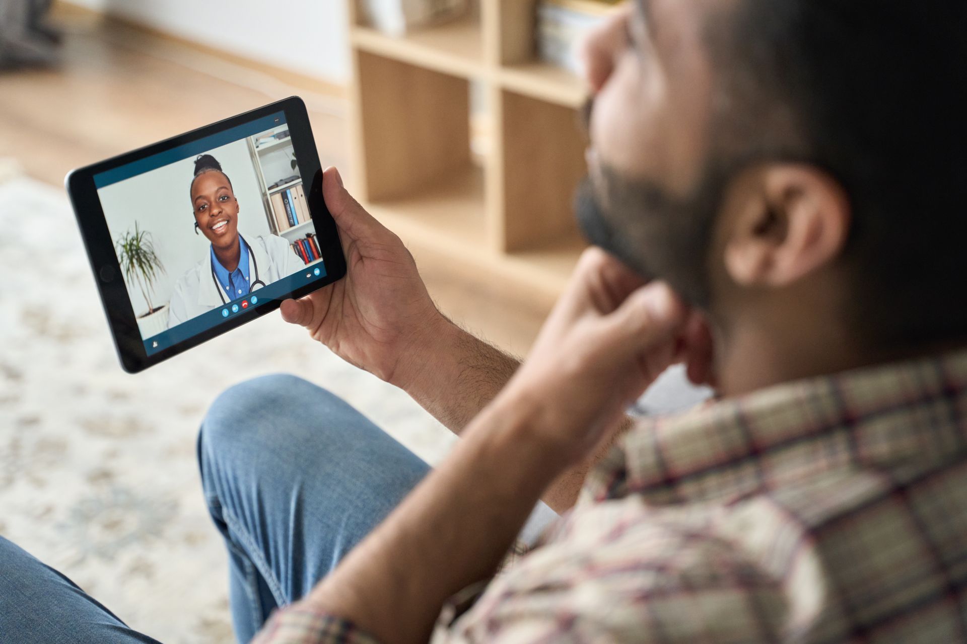 Man in plaid shirt on video call with a doctor on a tablet.
