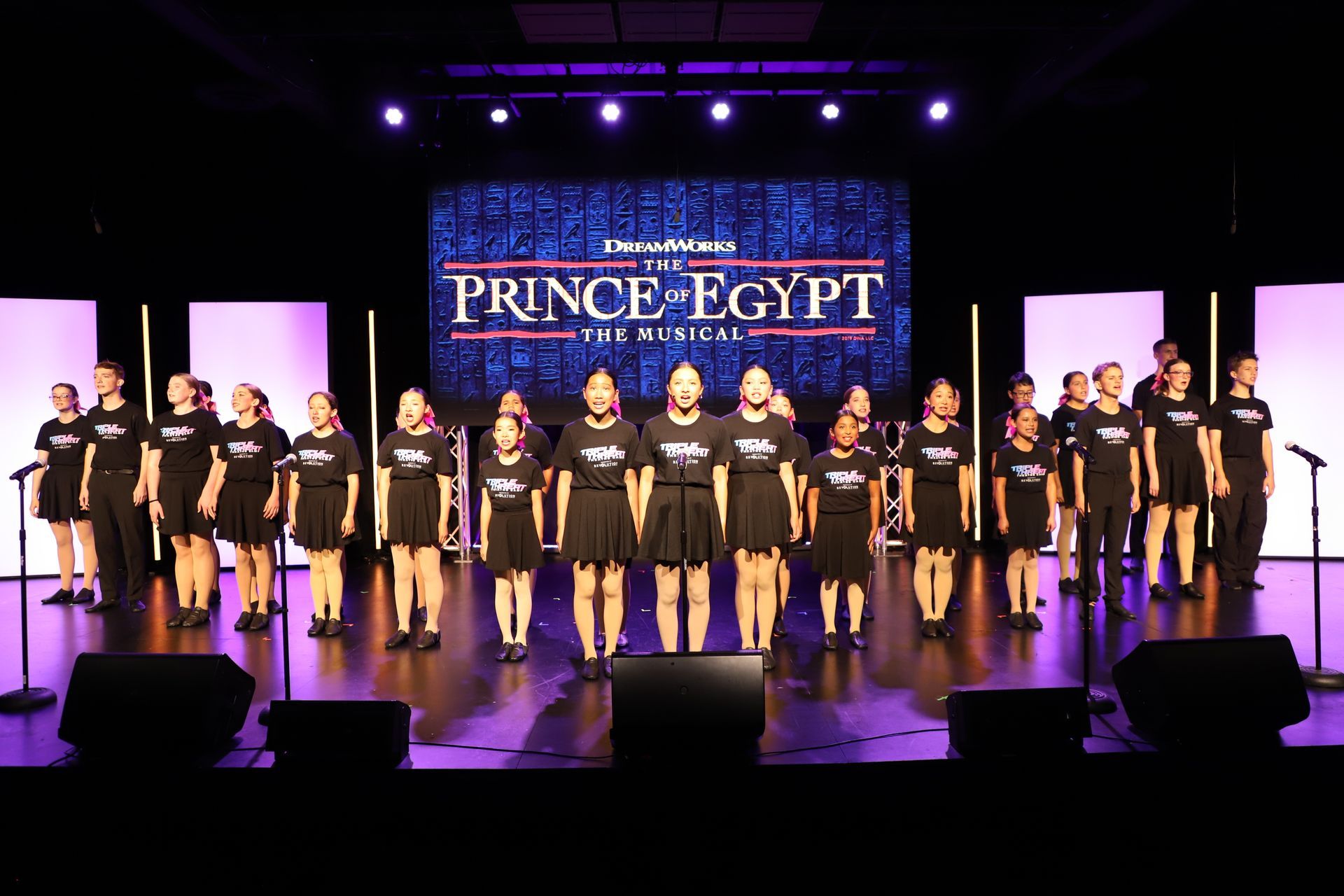 Choir on stage under purple lights with “Prince of Egypt” displayed on the screen behind them for a theater showcase.
