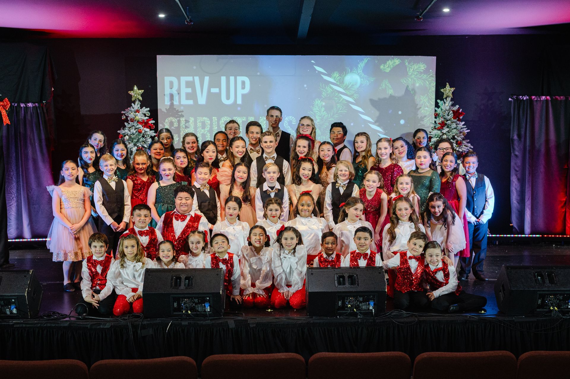 Large group posing on a stage with a “REV-UP” banner and colorful lights