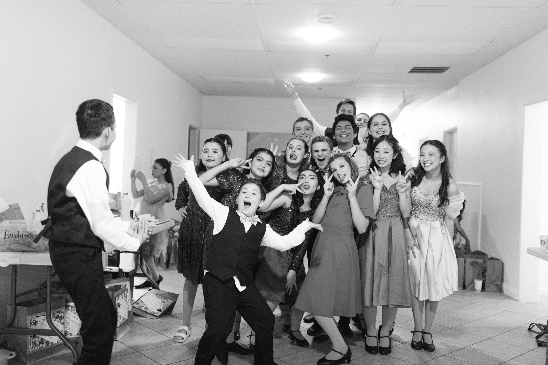 Group posing and dancing in a hallway while one person faces them with arms outstretched.
