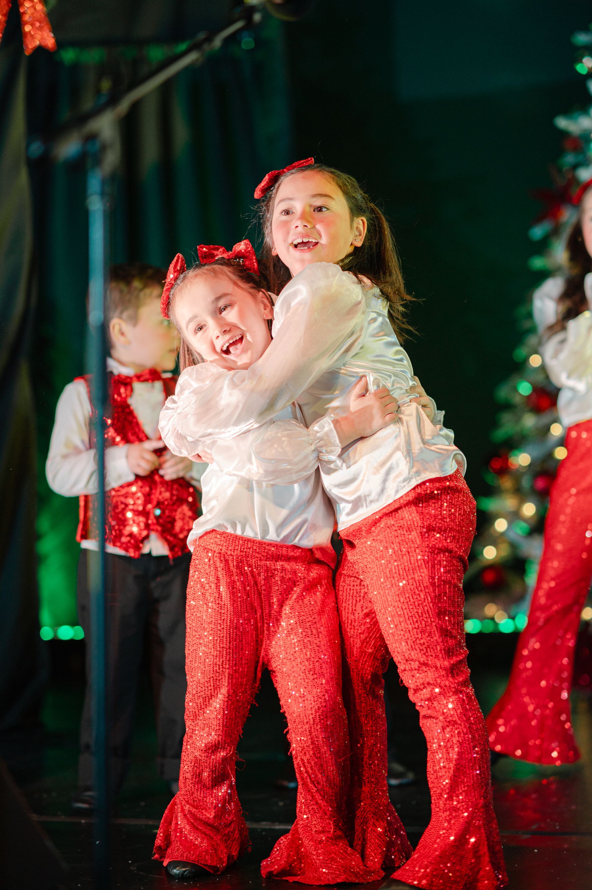 Two dancers in white tops and red pants pose onstage, smiling in festive lighting.
