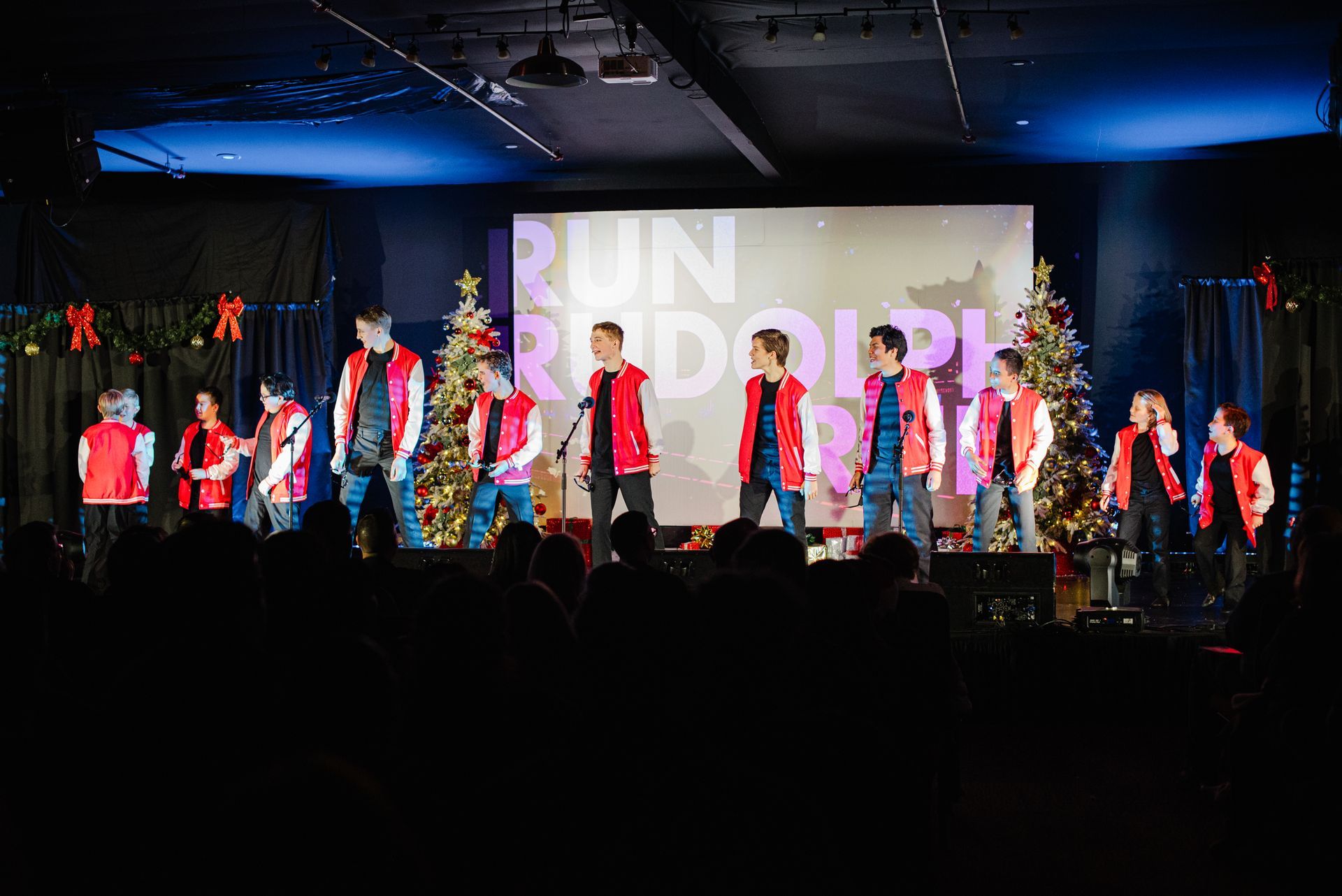 Group of performers in red and blue on a lit stage with a projected “RUN” backdrop