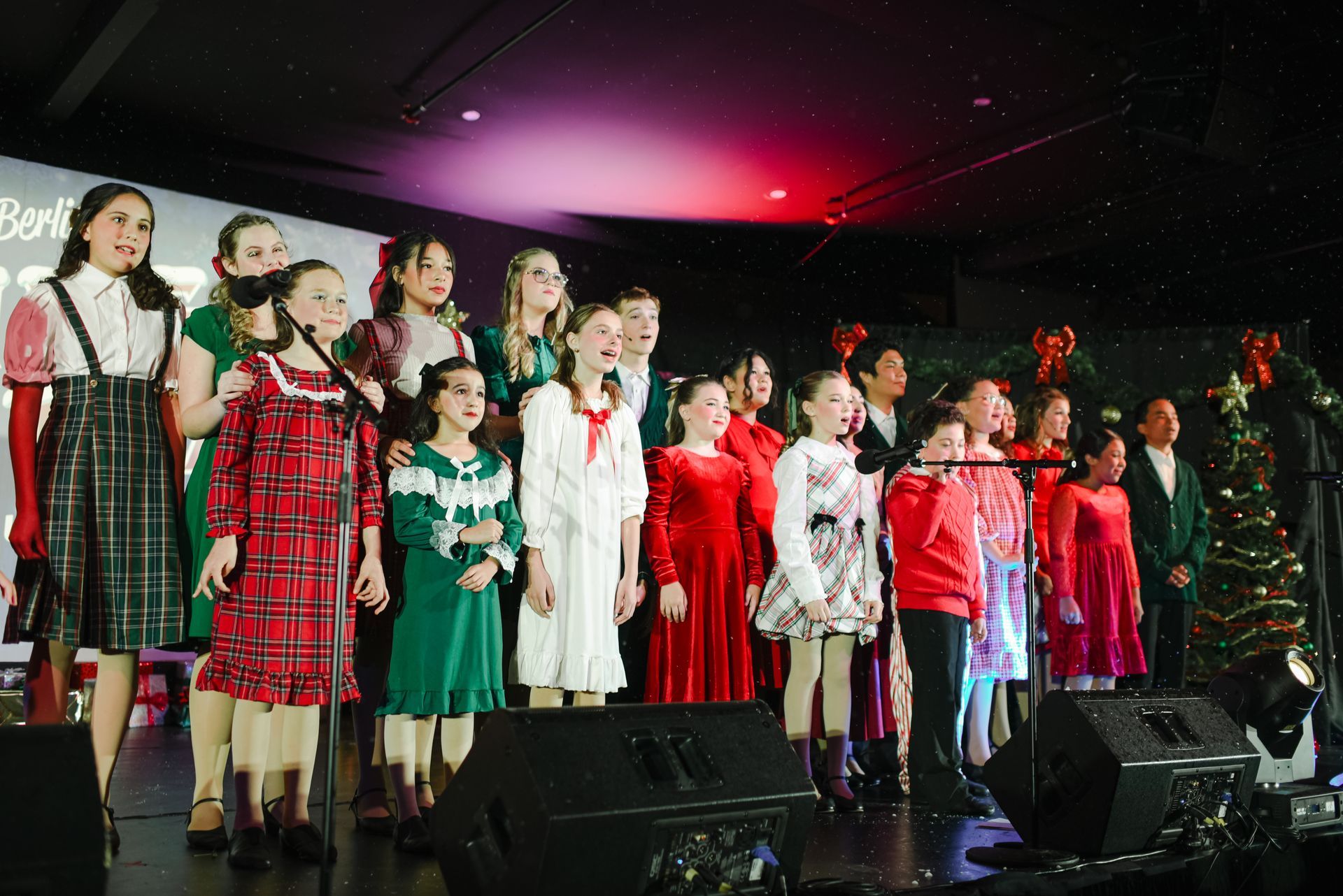 Choir of performers in festive dresses singing on a stage with red and green lighting