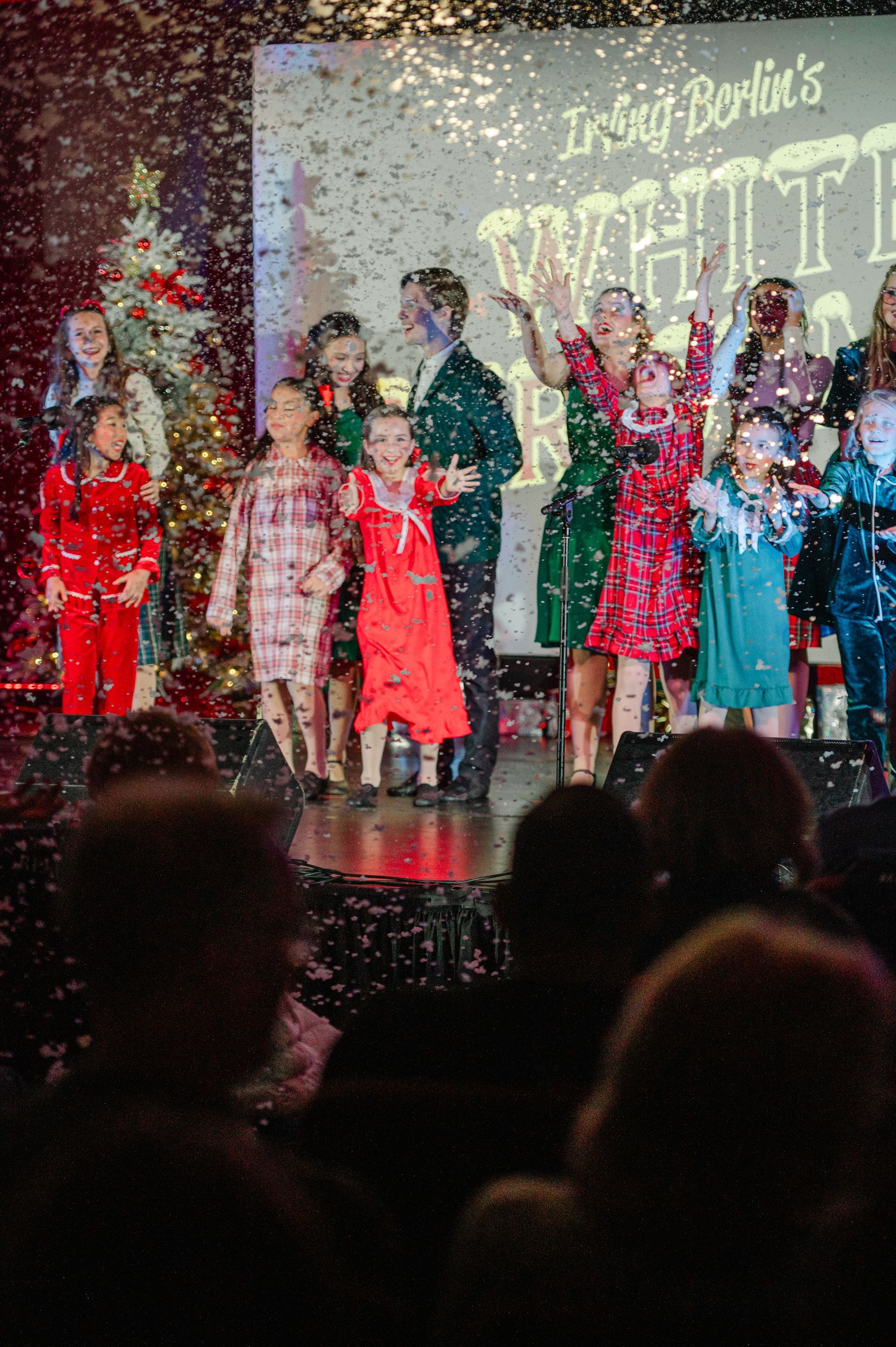 Children onstage in festive costumes with confetti falling during a holiday performance