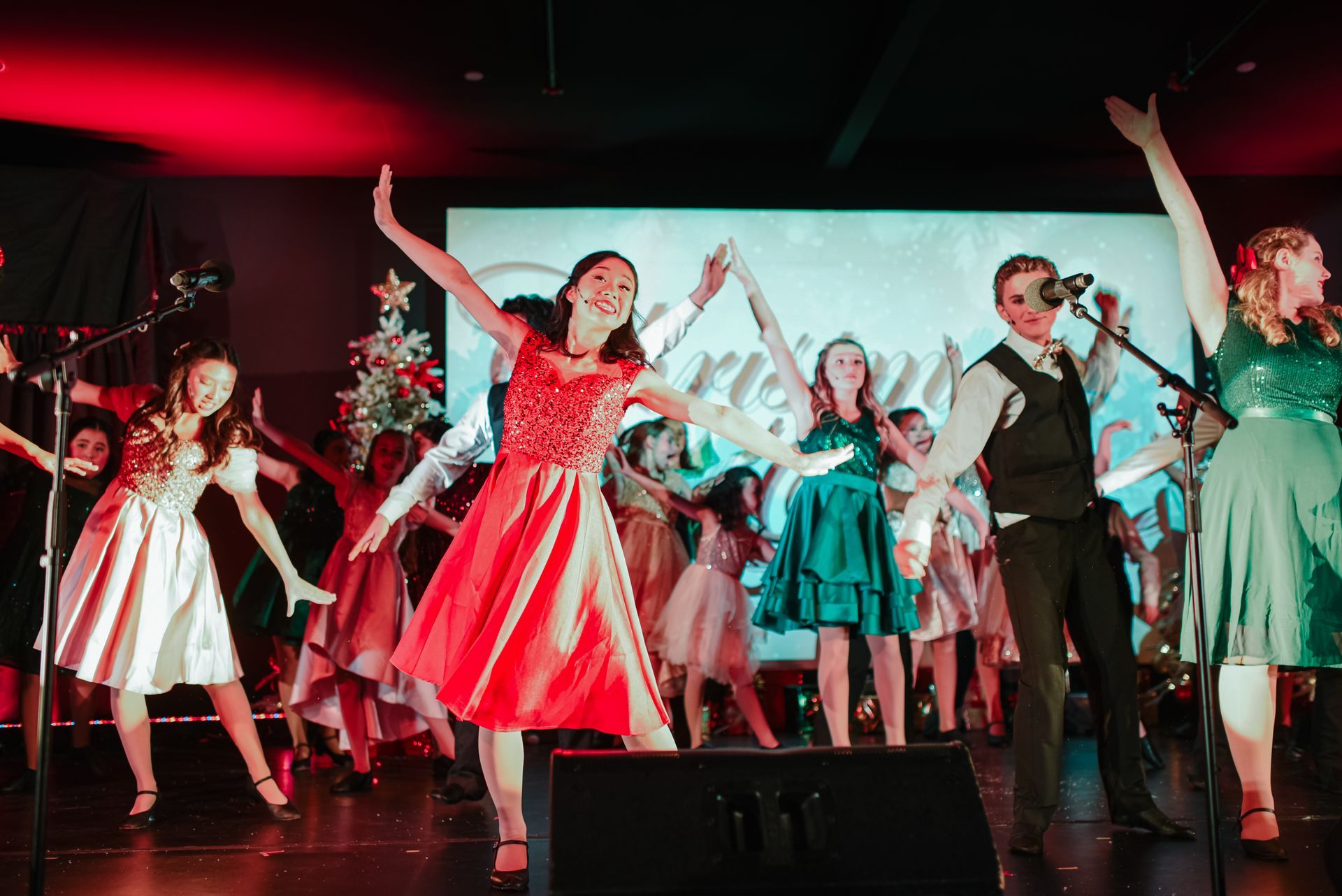 Costumed performers dancing onstage under colorful lights, with a Christmas tree in the background