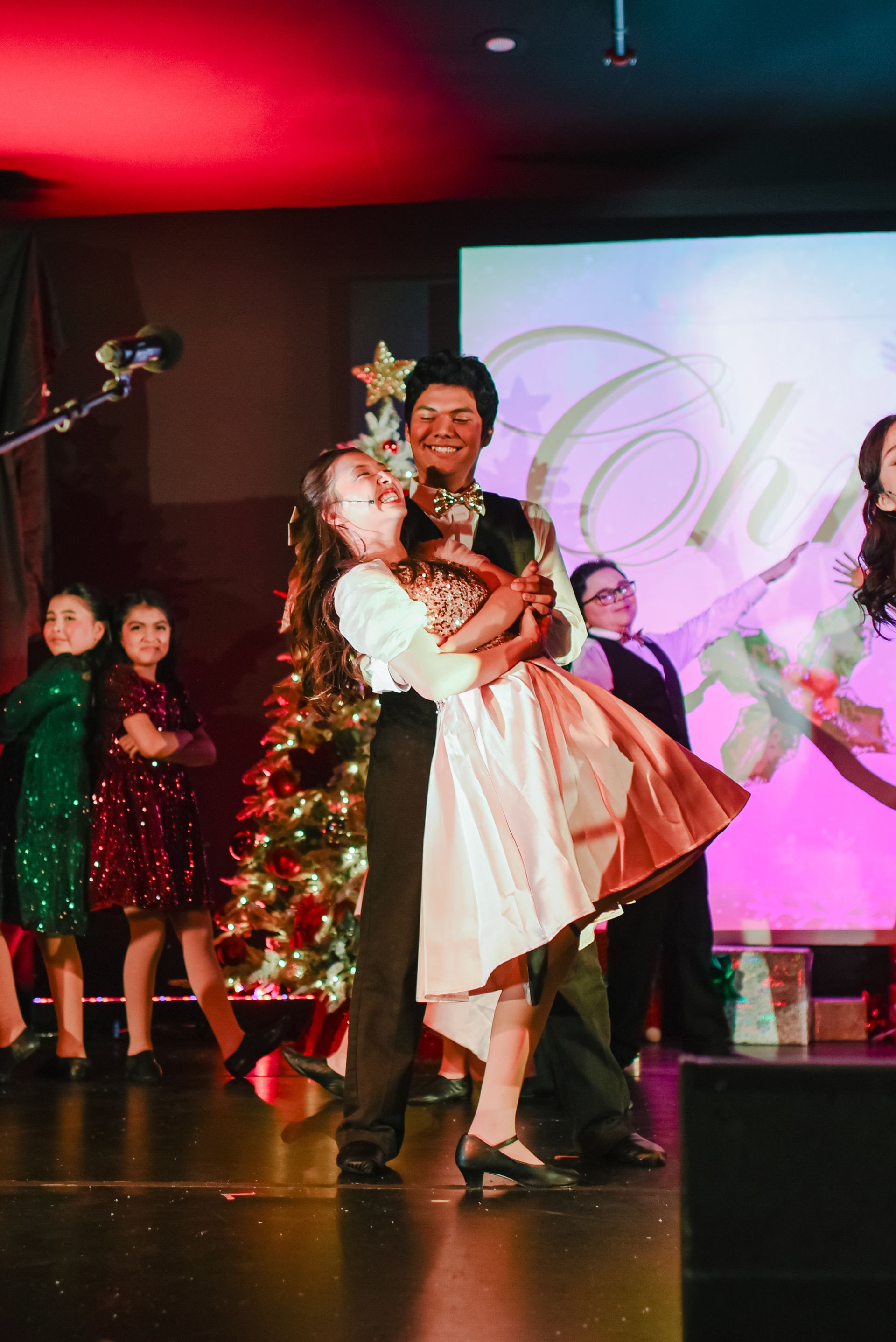 Couple dancing on a stage with holiday decorations and a Christmas tree in the background