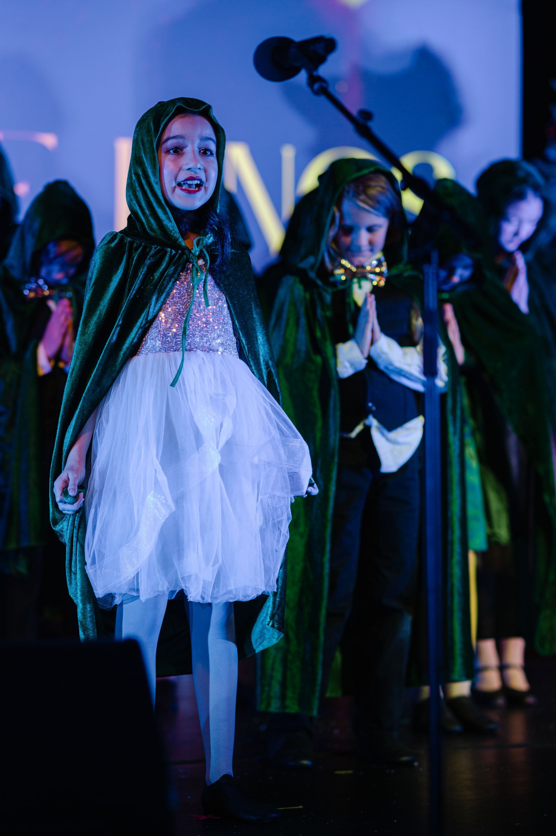 Children in costumes singing on a stage under blue-purple lights