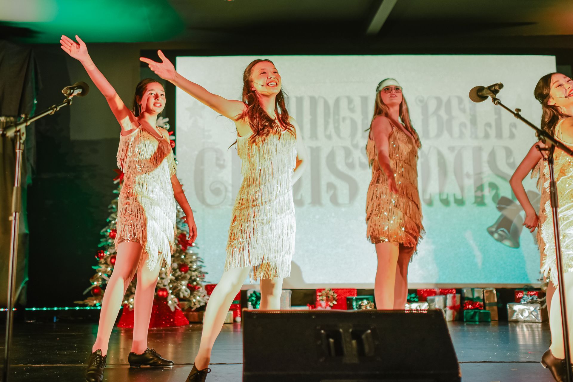 Three dancers in sparkly dresses perform on a stage with microphones and green lighting