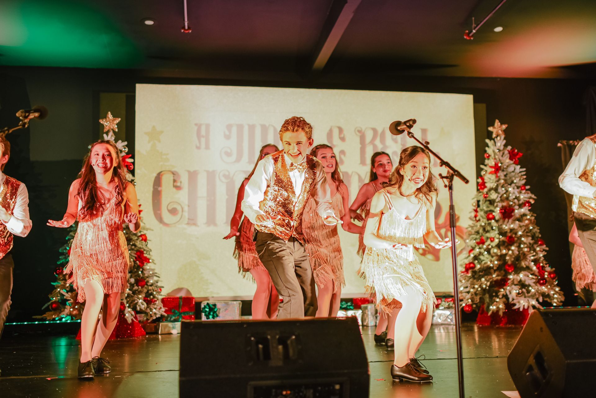 Four performers dancing on a lit stage with Christmas trees and a holiday backdrop