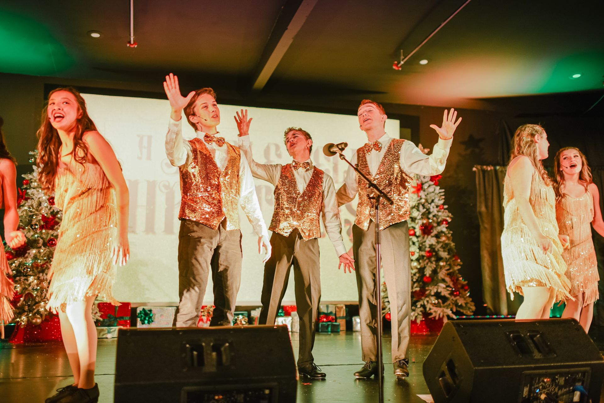 Performers onstage in metallic costumes, singing and dancing under colorful stage lights