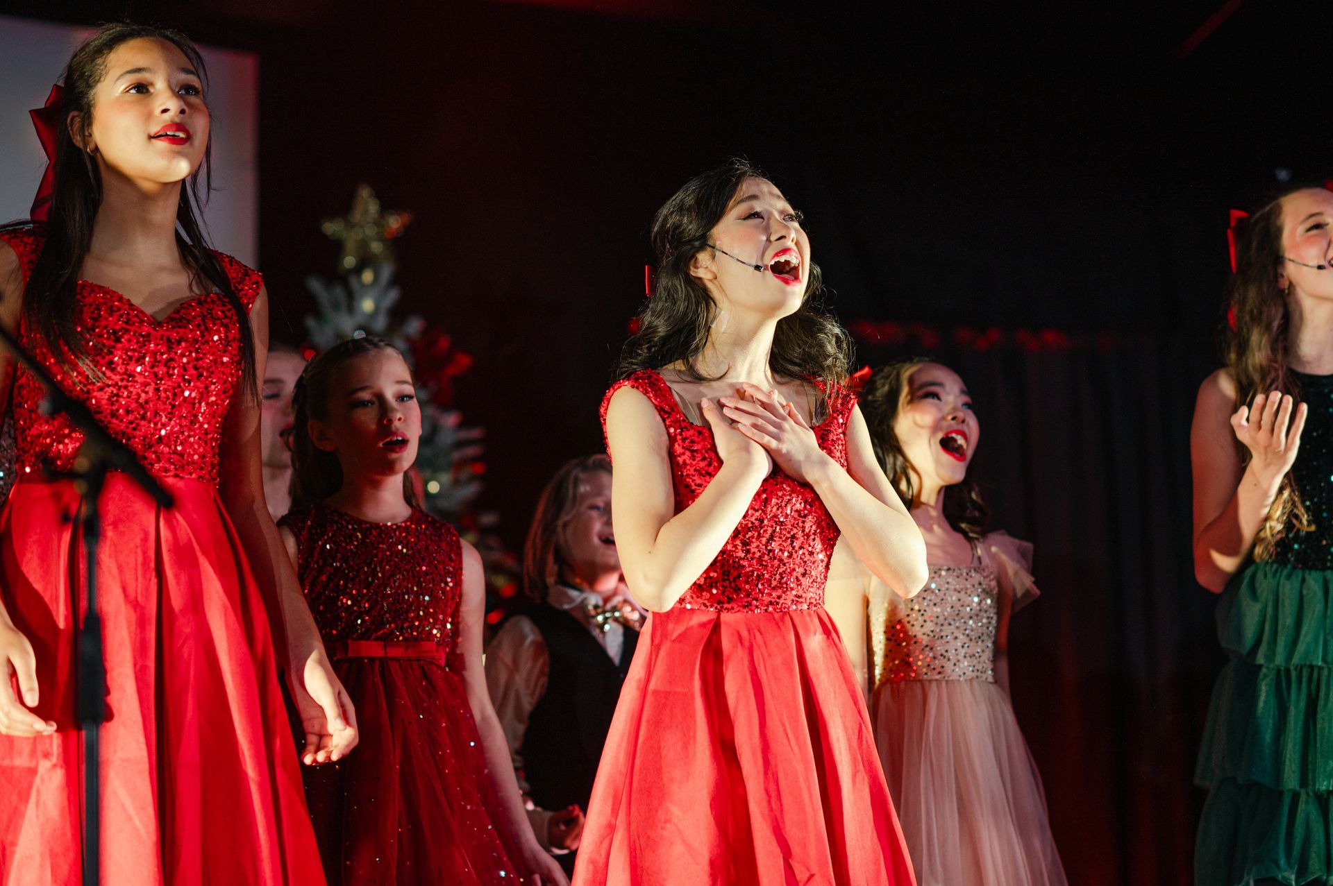 Performers in red dresses singing on a stage under red lighting