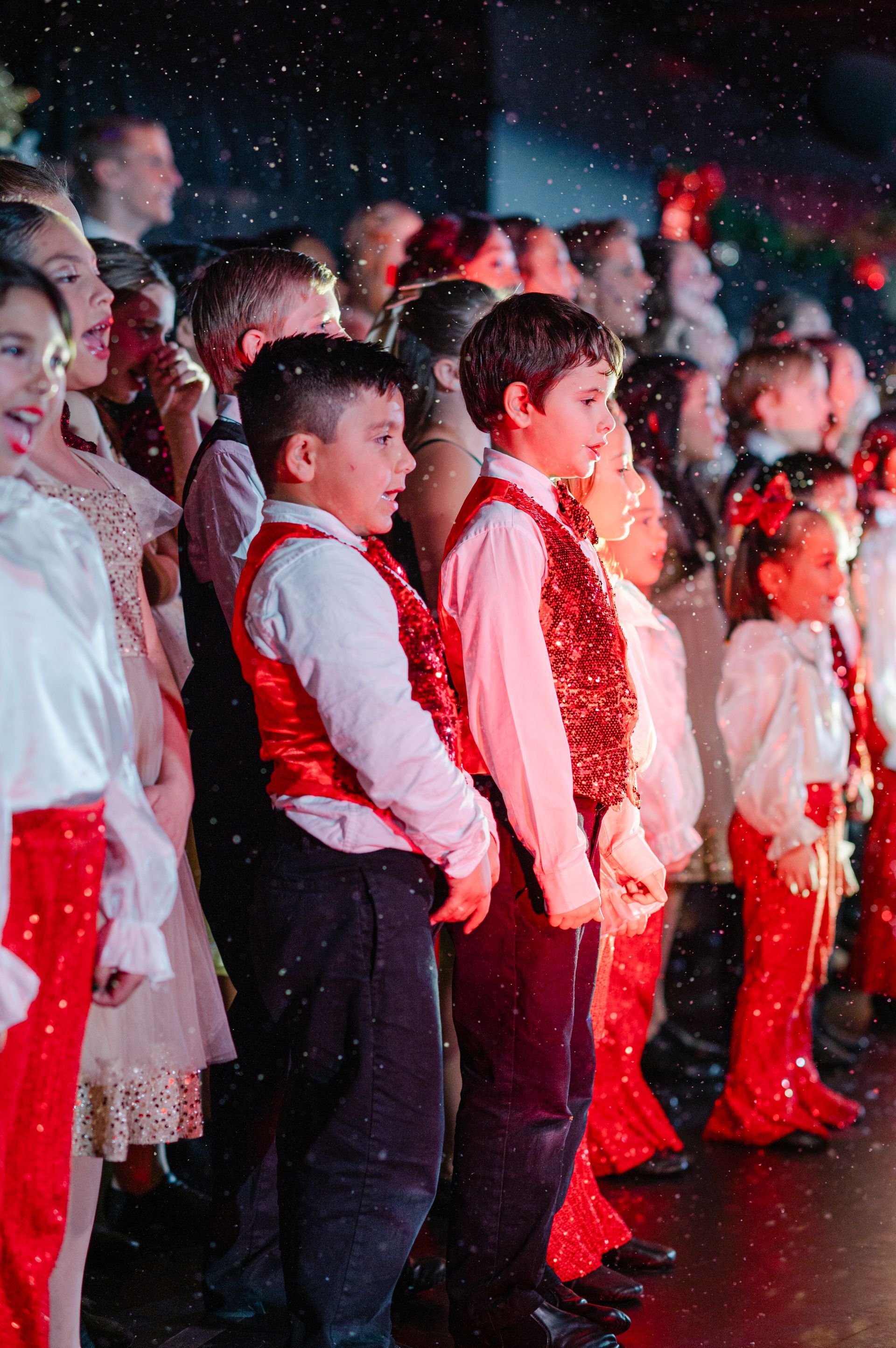 Children in red and white outfits standing in a row during a stage performance with falling confetti