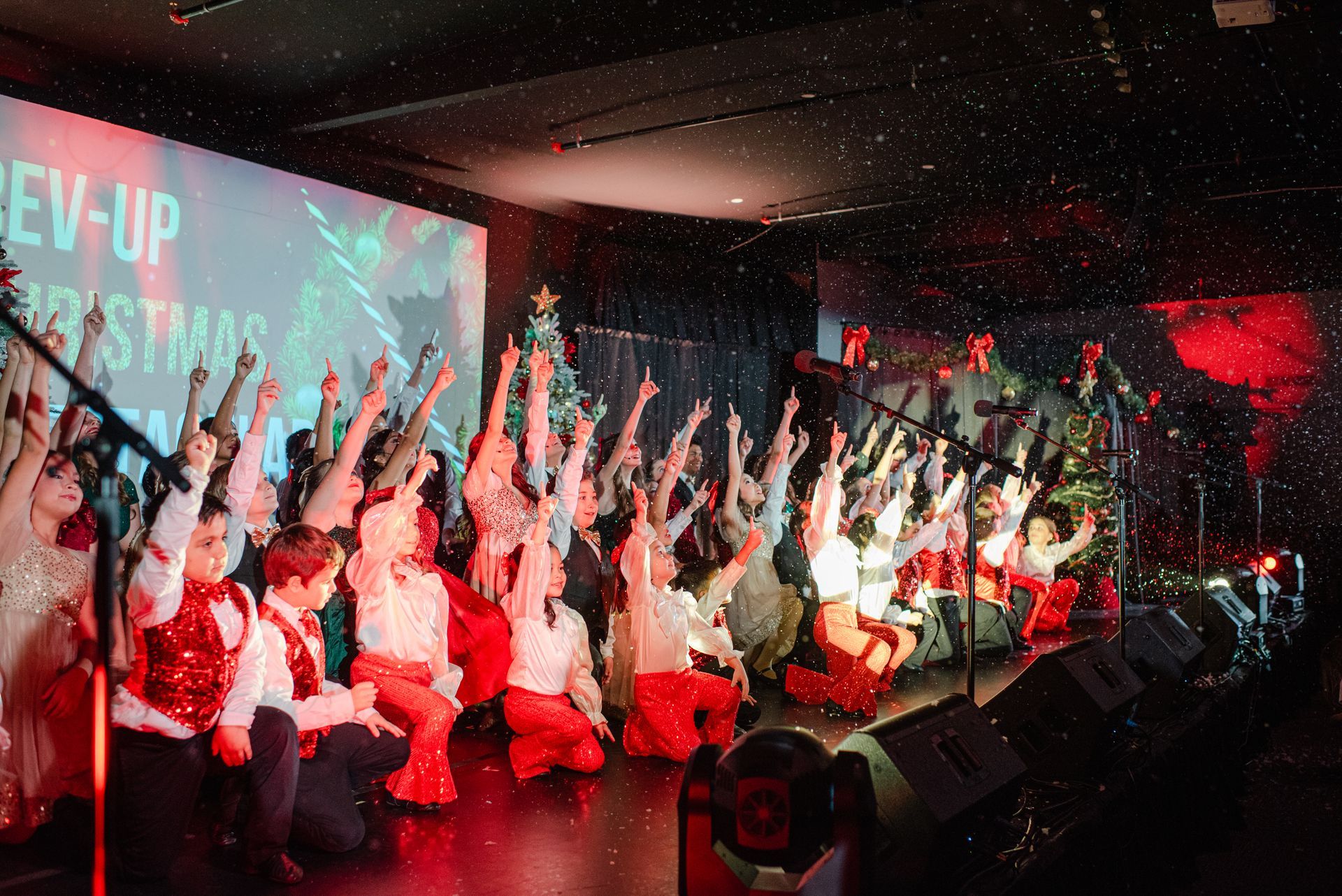 Crowd on stage with raised hands under red lights at a live event
