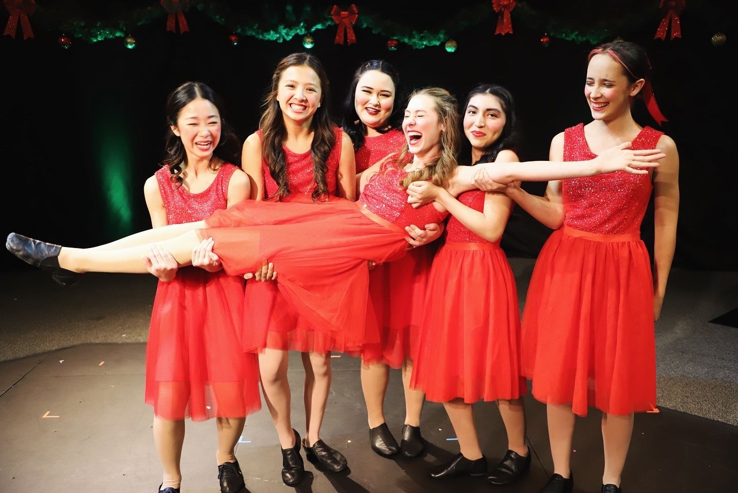 A group of young women in red dresses are standing next to each other on a stage.