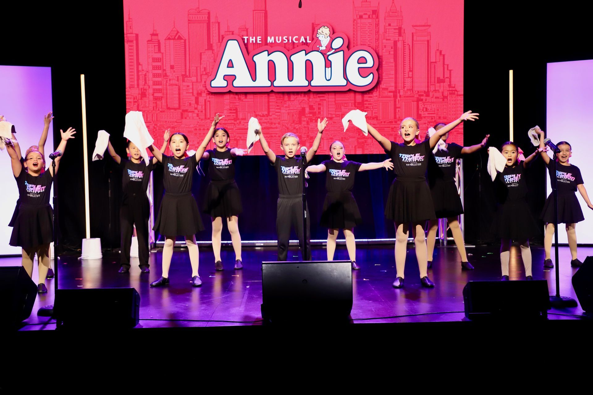 Cast of Annie bows onstage in front of a pink backdrop with the title 