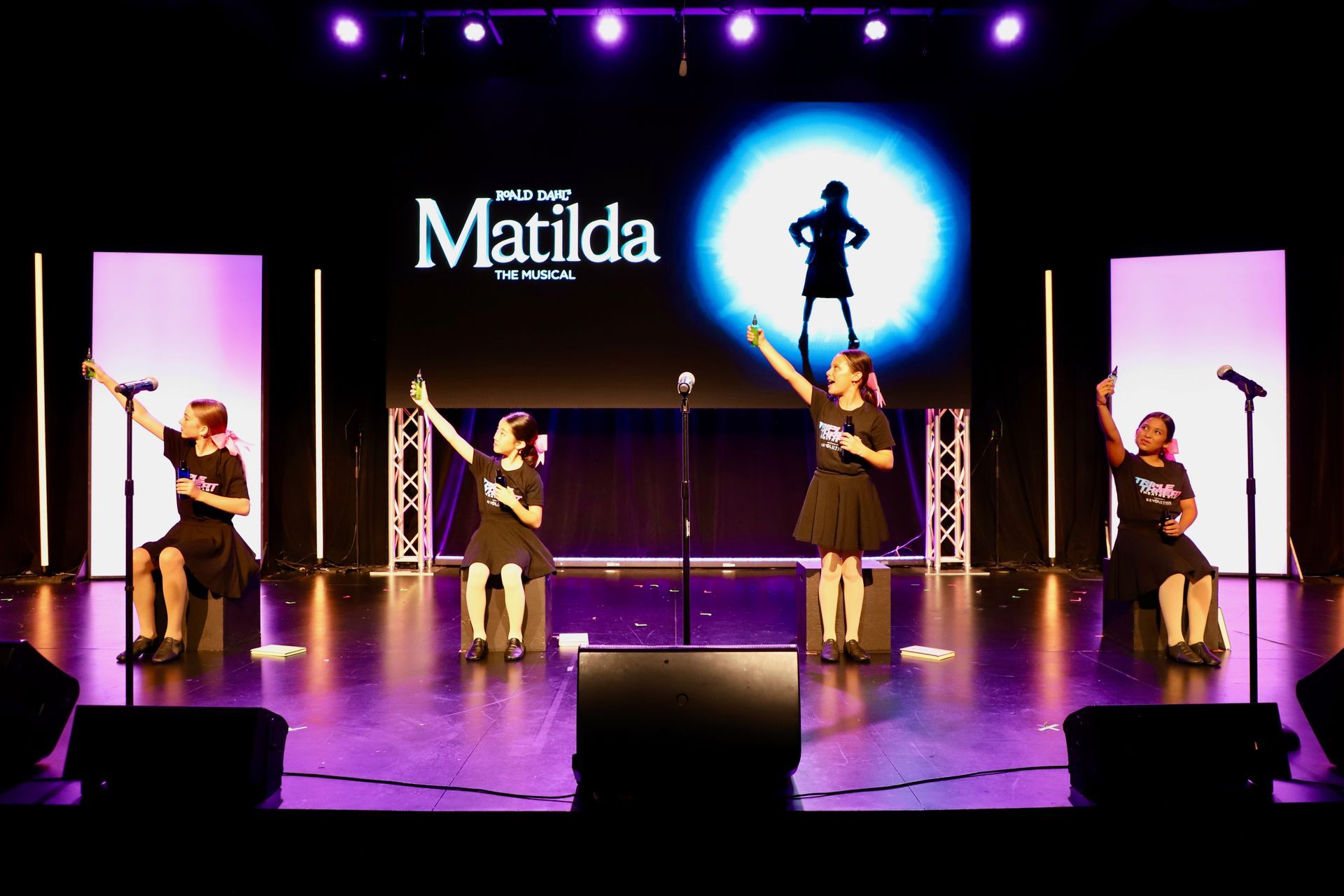 Stage performance of Matilda with four performers and a glowing blue silhouette backdrop for a theater showcase.