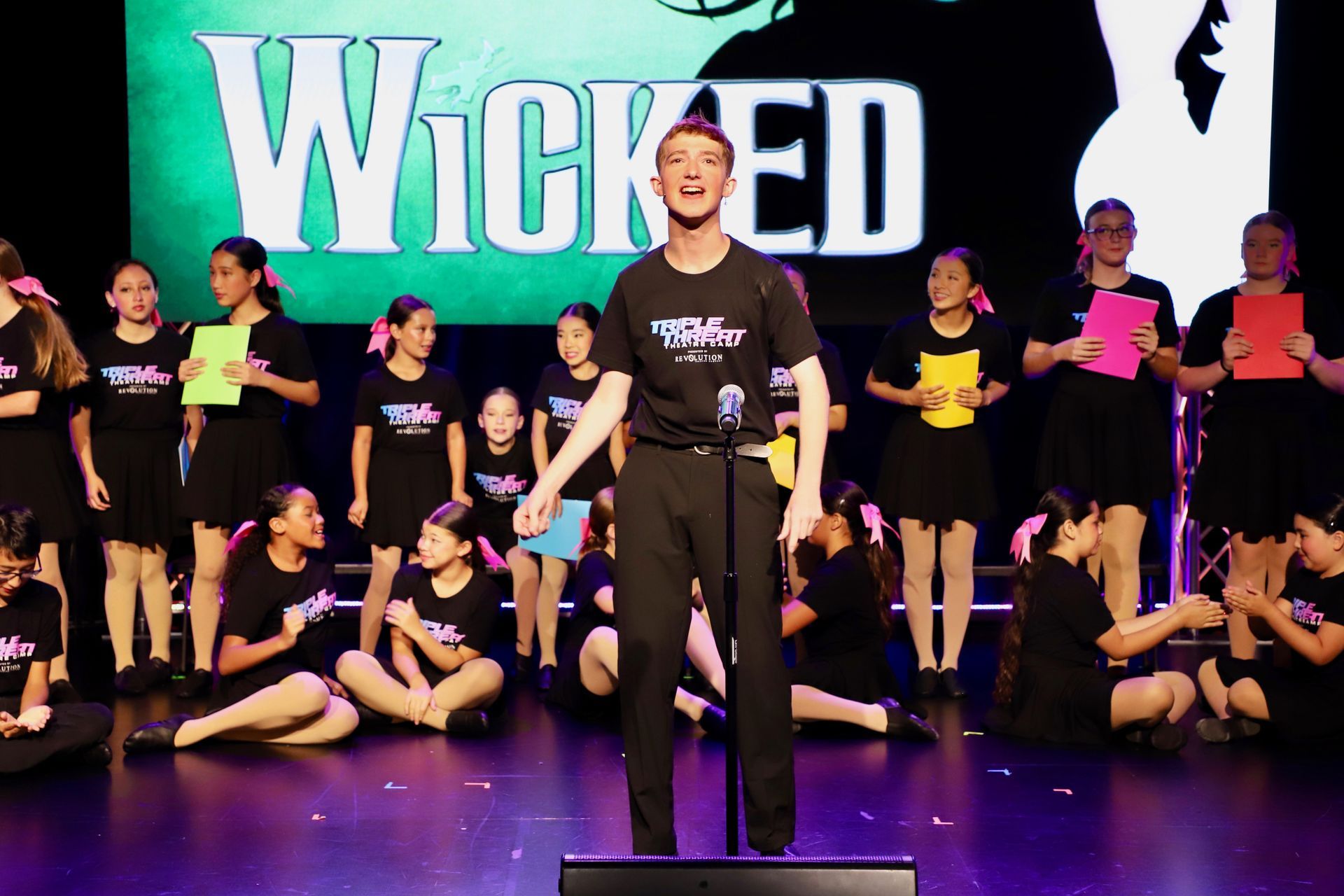 Stage performance of dancers in front of a Wicked backdrop for a theater showcase.