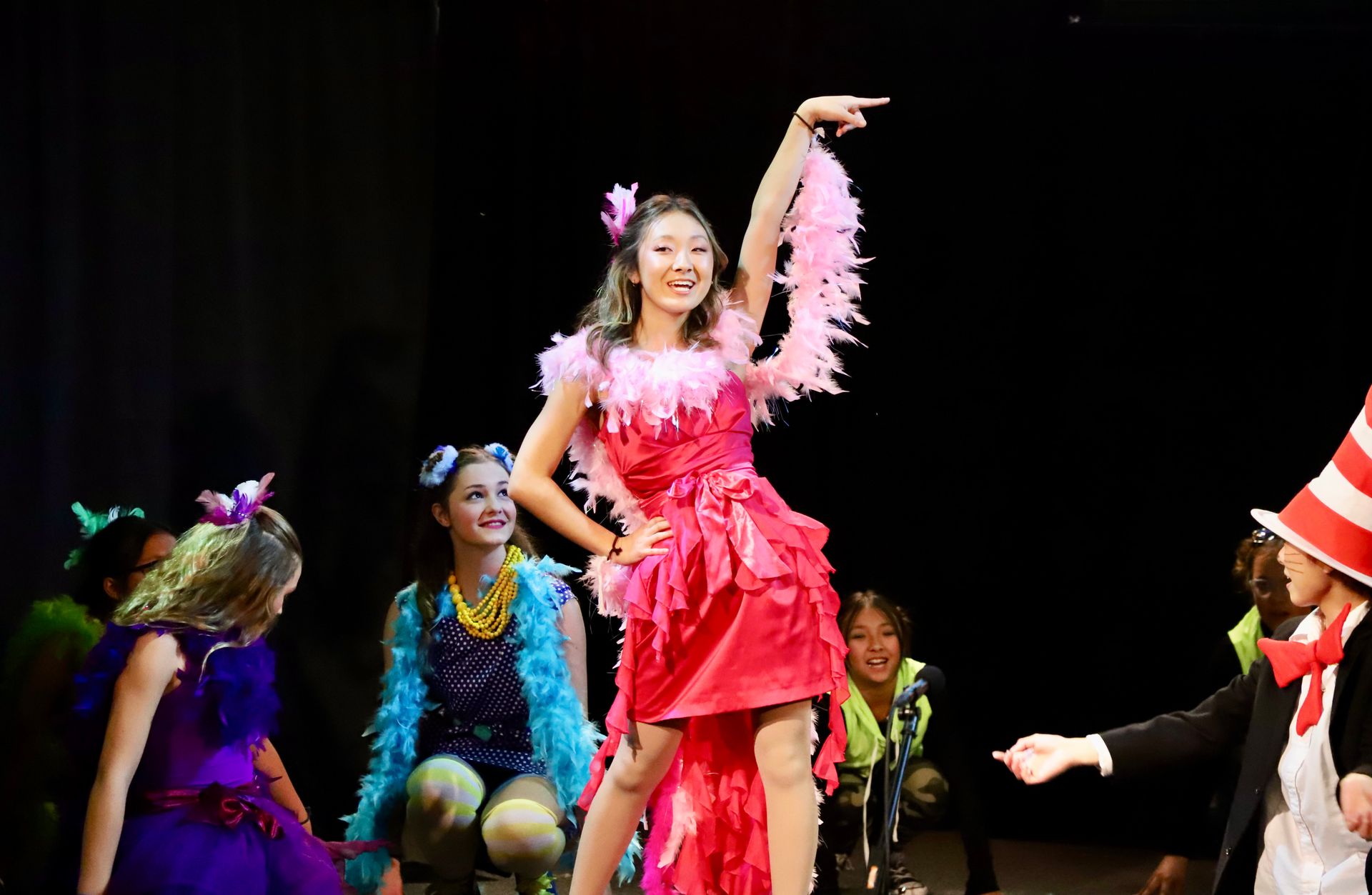 A woman in a pink dress is dancing on a stage with other people.