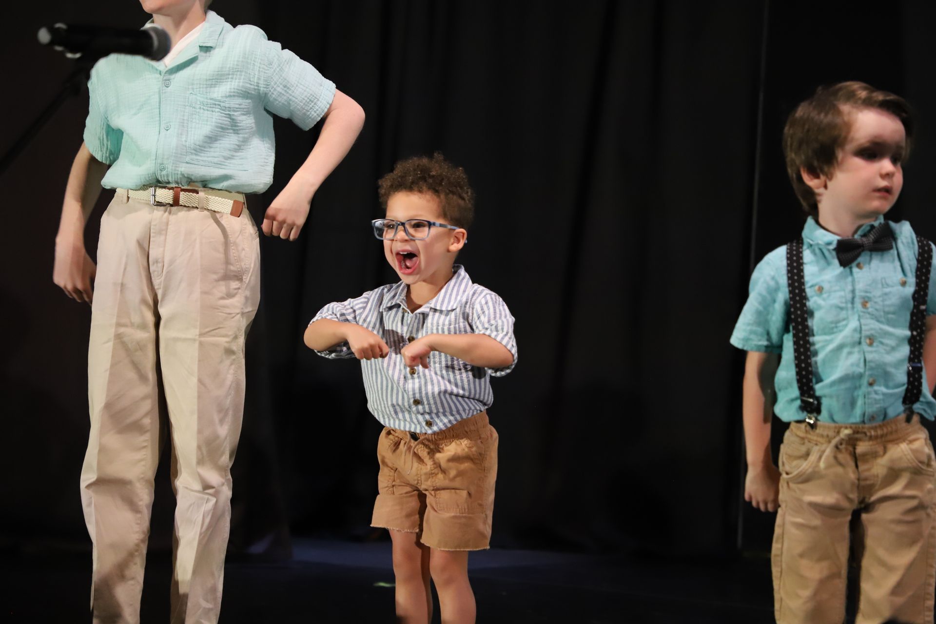 Three performers on a stage in mint shirts and khaki pants, for a theater performance.